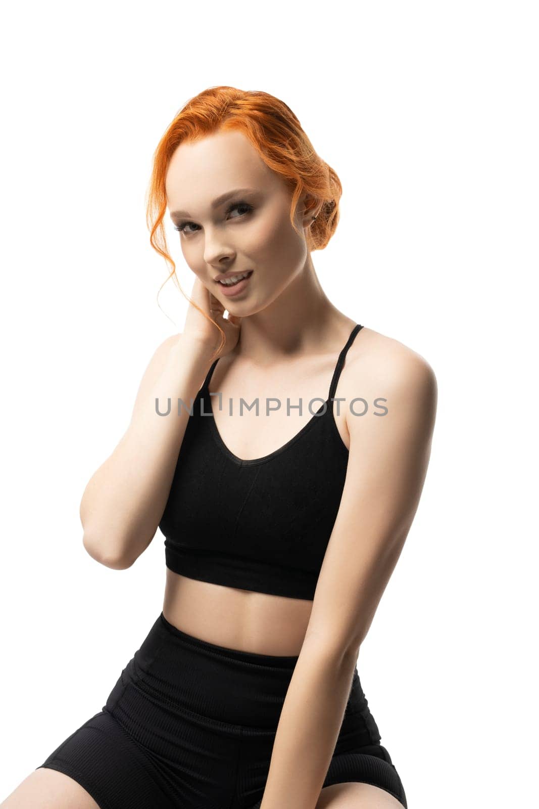 Self assured young fit female model with ginger hair in black sportswear smiling look at camera isolated