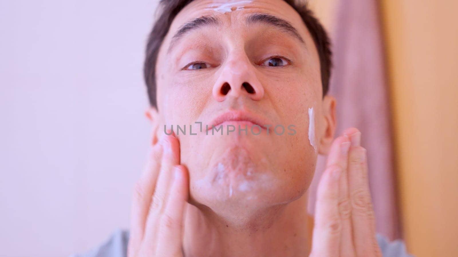 Caucasian man applying moisturizing cream on his face in the bathroom
