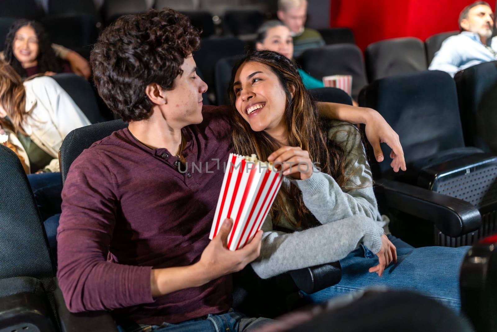 Happy couple sharing popcorn and enjoying a movie at the cinema, embracing during a romantic date