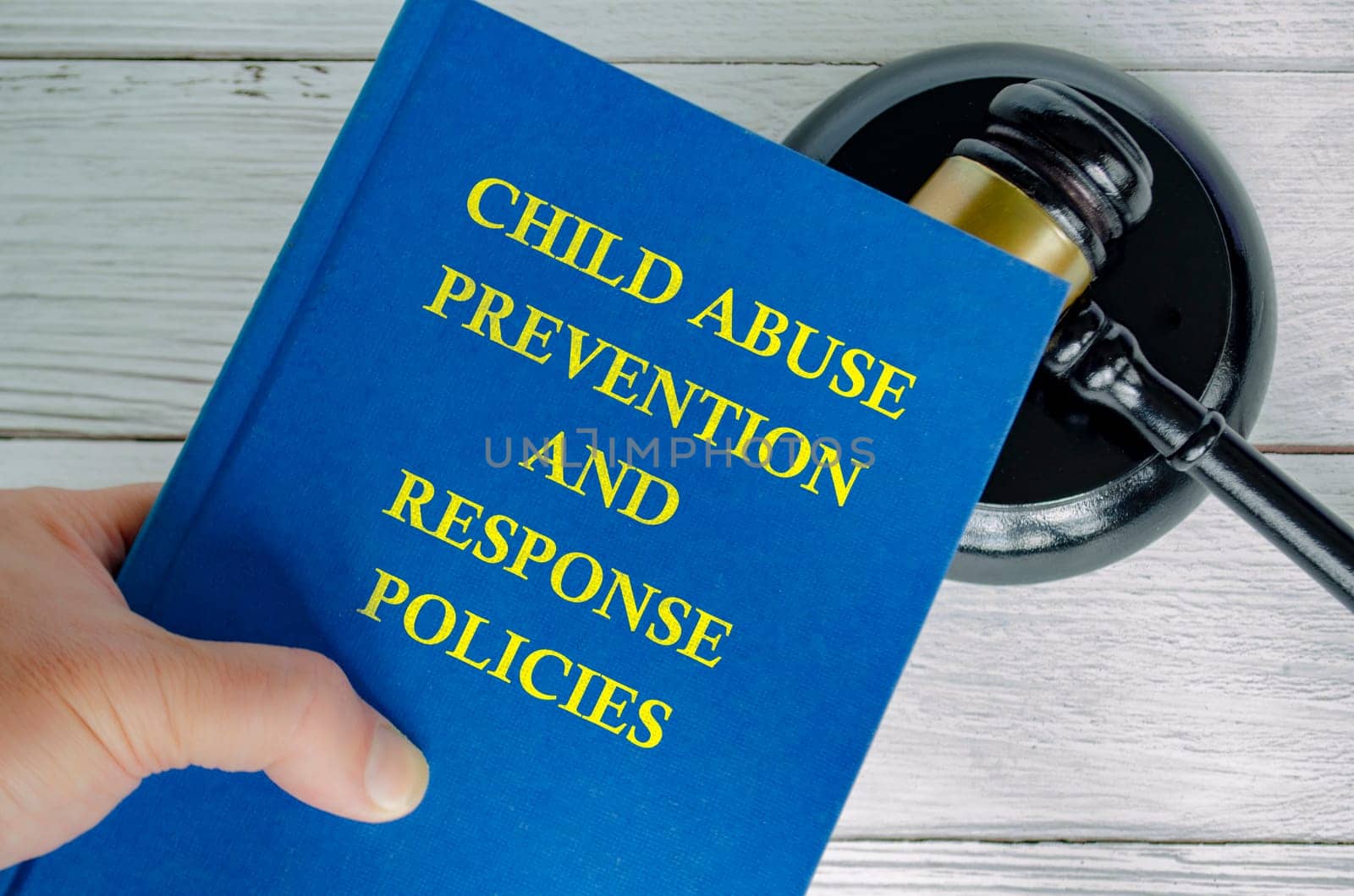 Hand holding Child Abuse Prevention and Response Policies book with gavel background.
