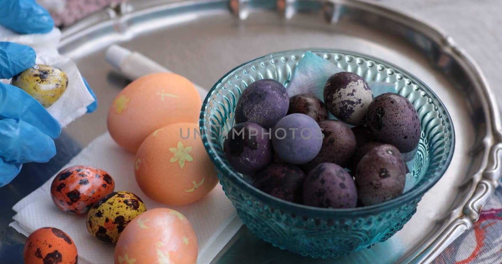 Colorful Easter eggs and unique quail eggs sit on a silver tray. The eggs, painted in vibrant hues, showcase intricate designs and invite festive joy.