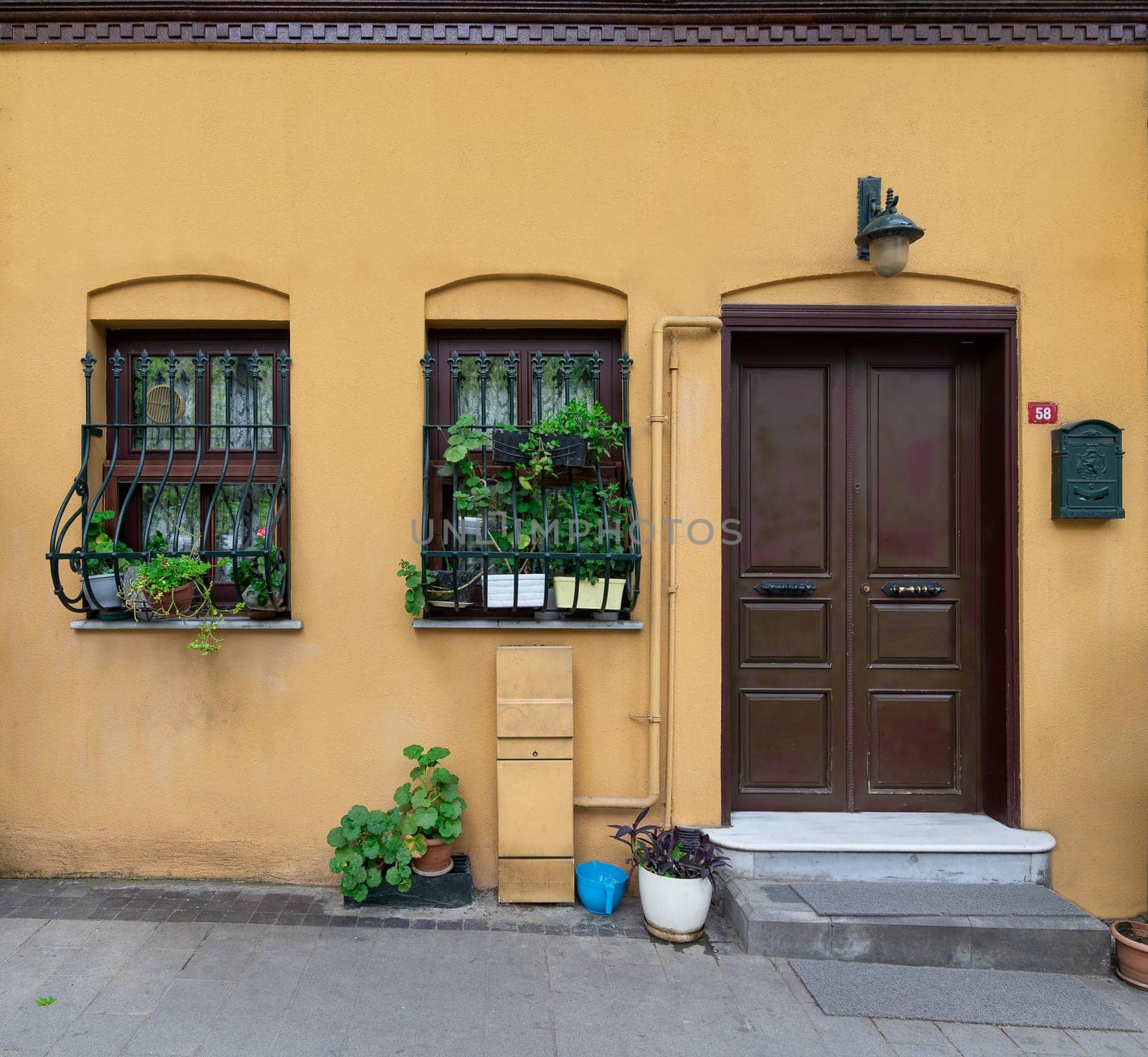 Facade of residential building with walls painted in orange, wooden door, and two wrought iron windows, at a narrow street, in Kuzguncuk neighborhood, Uskudar district, Istanbul, Turkey