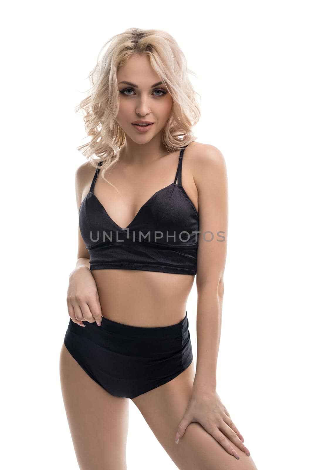 Alluring blond female wearing black underwear standing against white background in studio and looking at camera