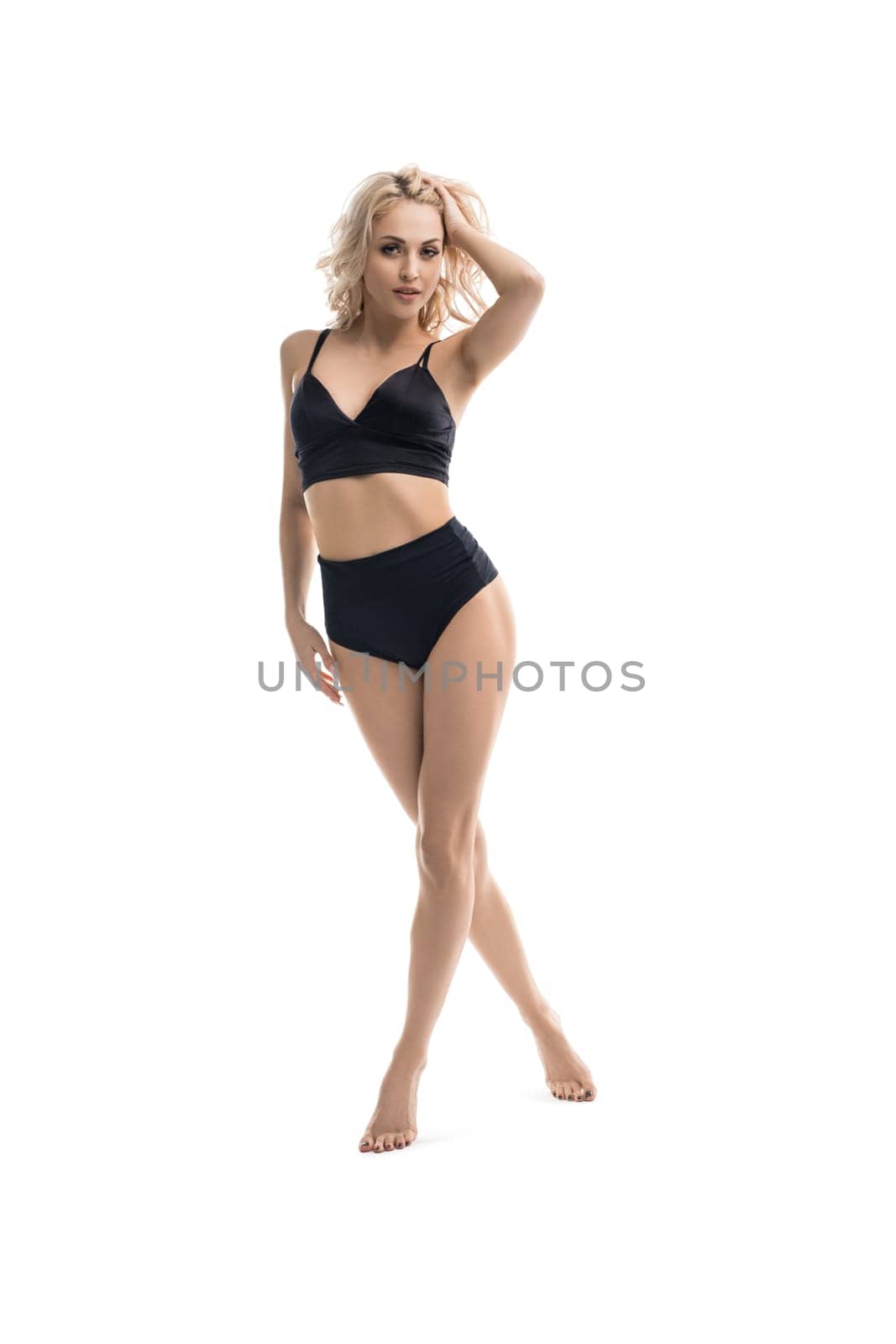Alluring blond female wearing black underwear walk against white background in studio and looking at camera