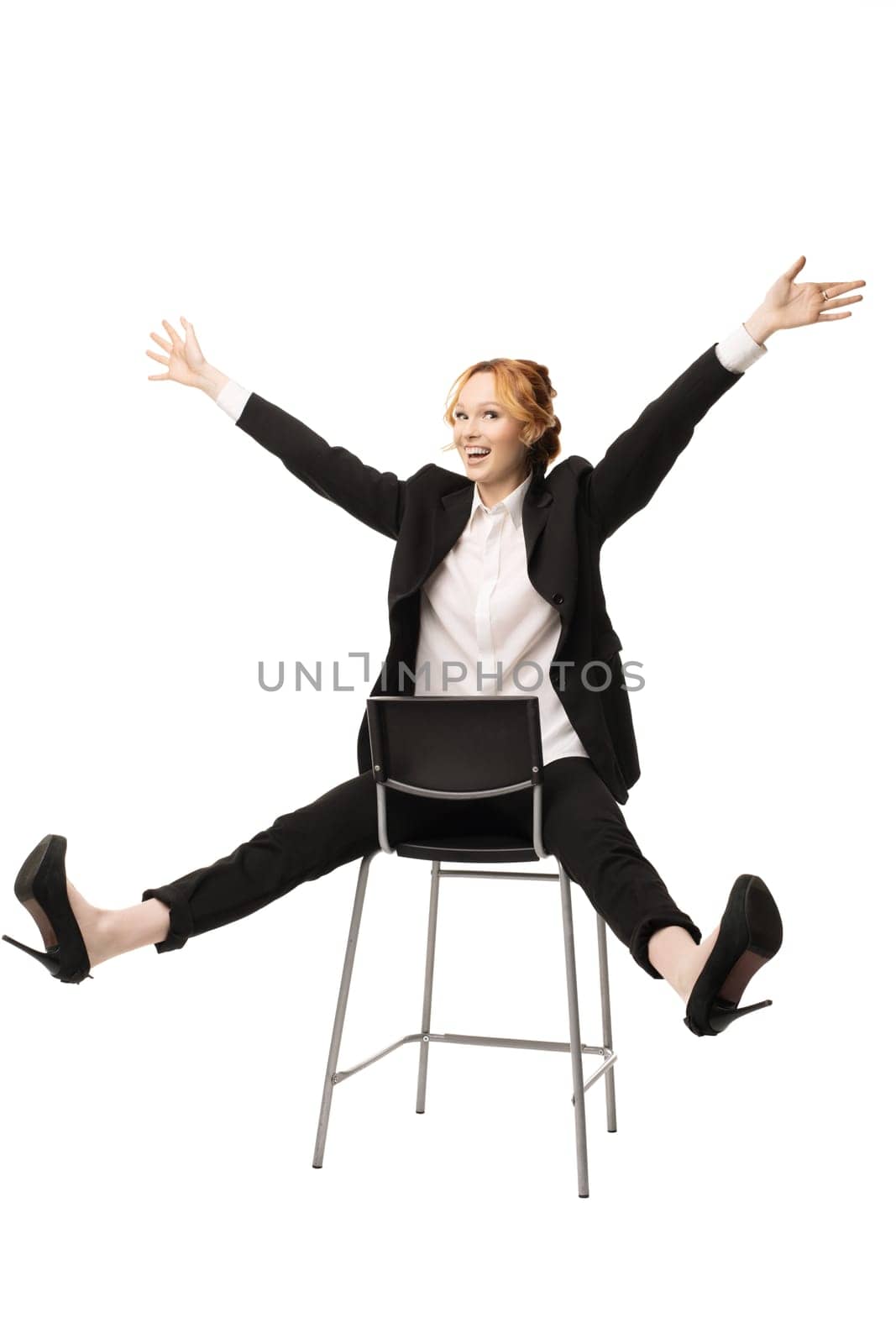 cheerful young excited female manager with ginger hair in formal suit smiling and looking at camera while sitting on chair with outstretched arms