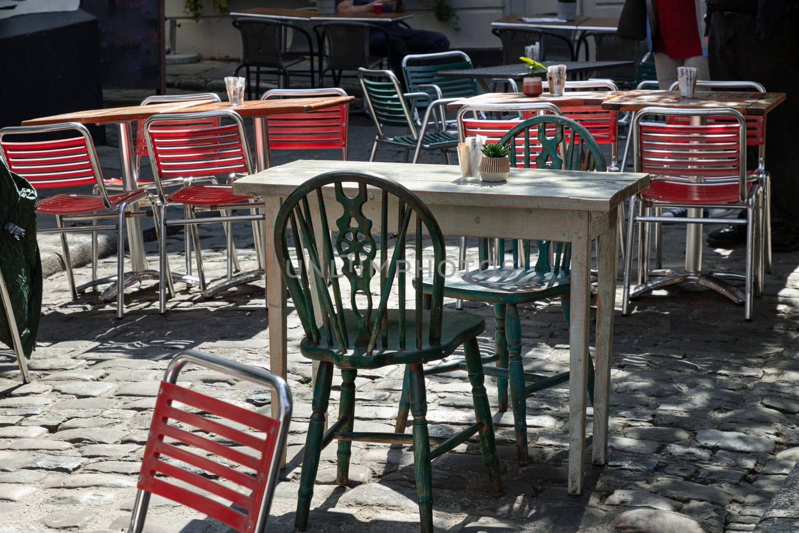 Windsor, UK - Apr 03, 2025 - Sunlight shine through Wooden table and Green metal chairs outside a cafe on street in the afternoon. use it as your Wallpaper, Poster and Space for text, Selective focus.