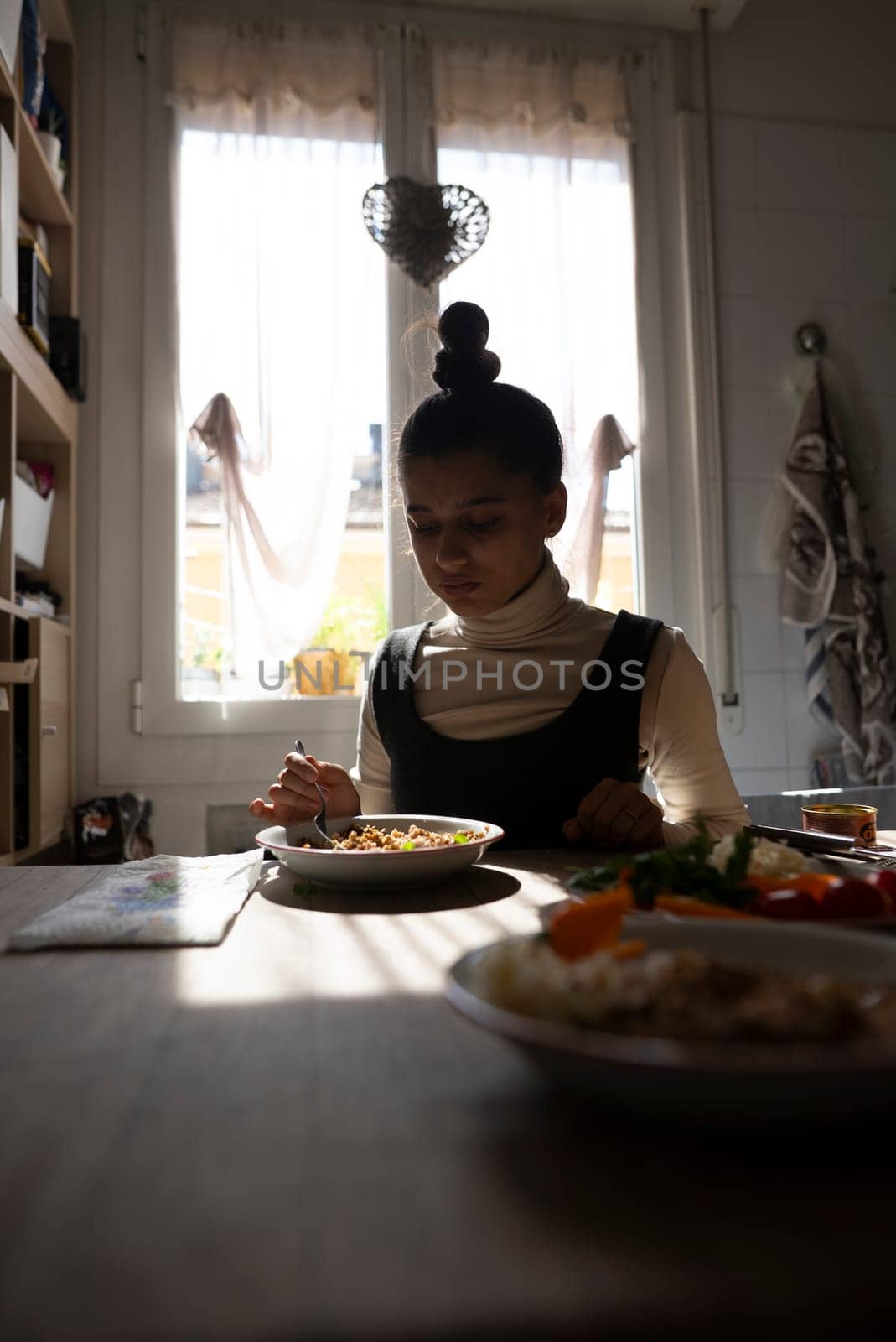 A woman delicately enjoys her meal within a cozy and warmly lit dining space, showcasing a moment of deep tranquility