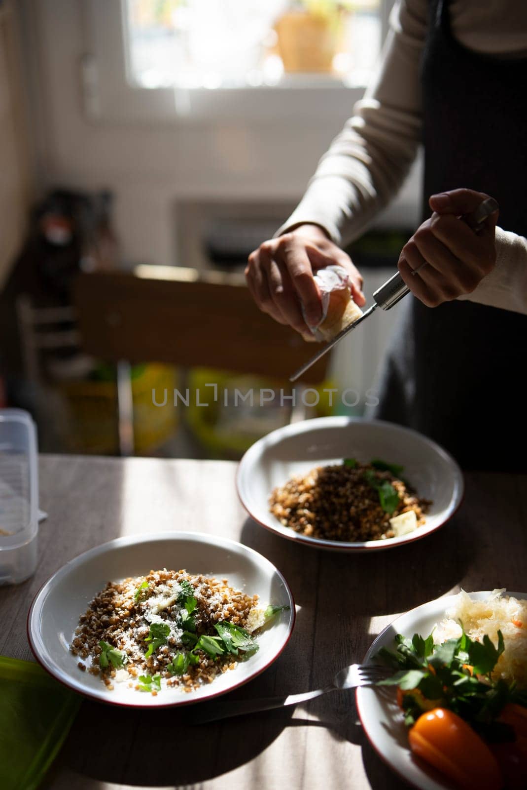 In a bright kitchen, a skilled cook garnishes two plates of delicious food with fresh herbs and spices