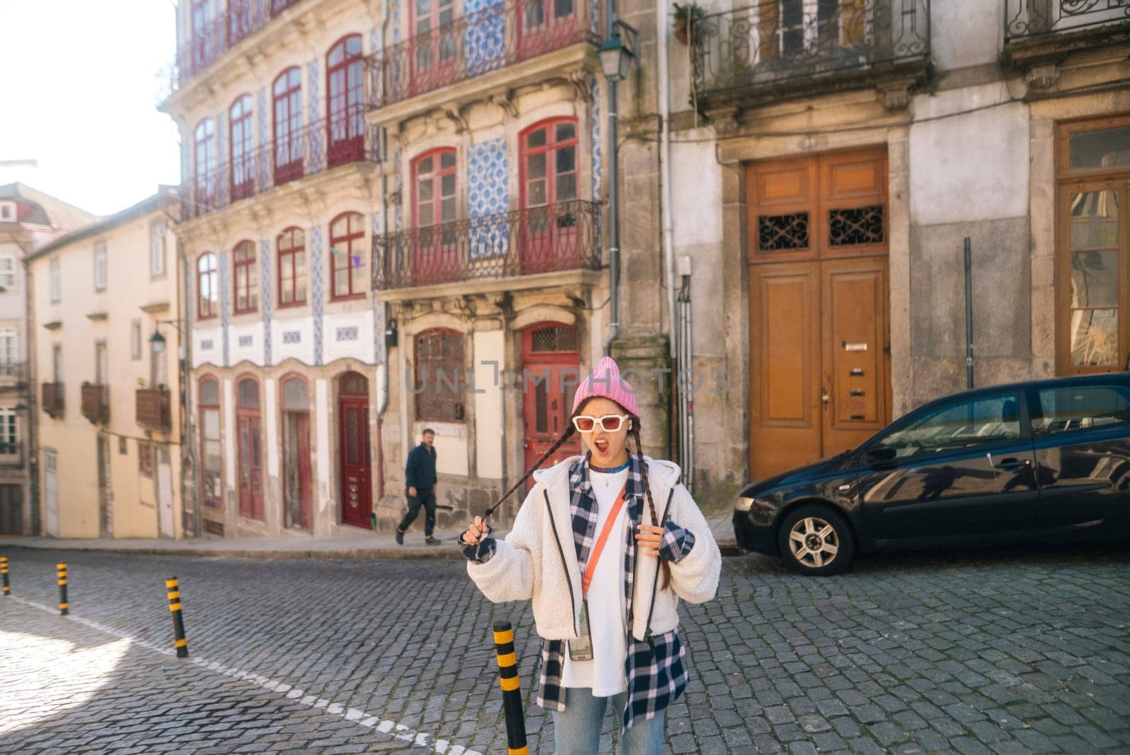 A very stylish individual confidently poses on a charming cobblestone street surrounded by colorful buildings