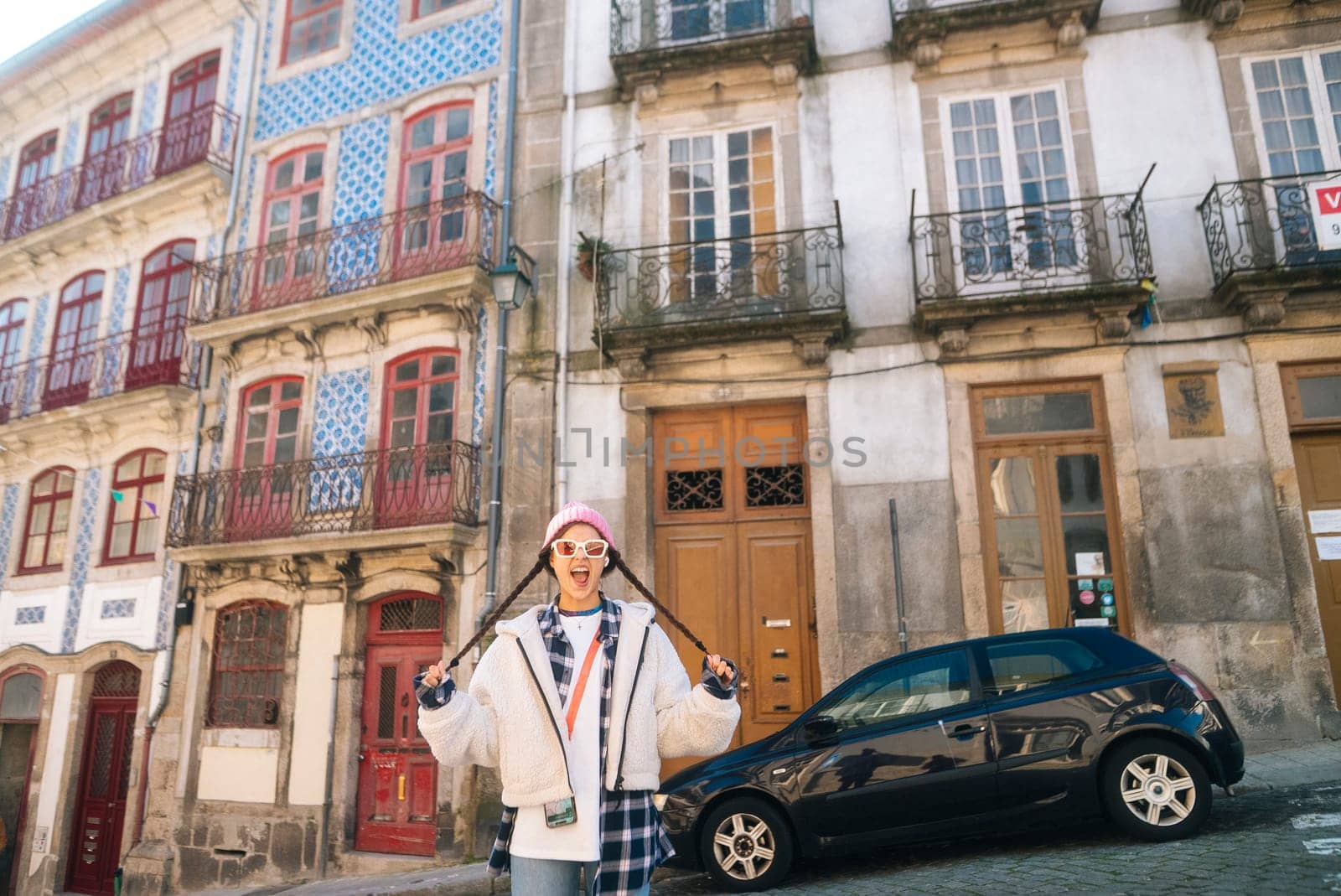 A stylish individual poses in front of vibrant buildings, showcasing modern fashion in an urban environment.