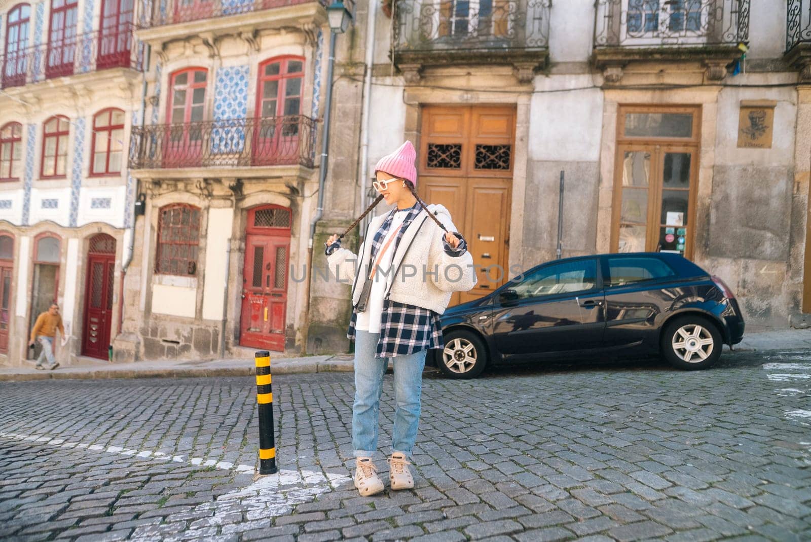 A stylish young woman confidently poses in a picturesque street scene that features beautiful vintage architecture