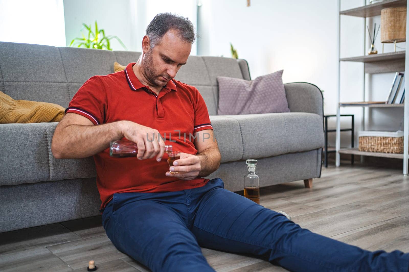 Mature man sitting on the floor and drinking alcohol.