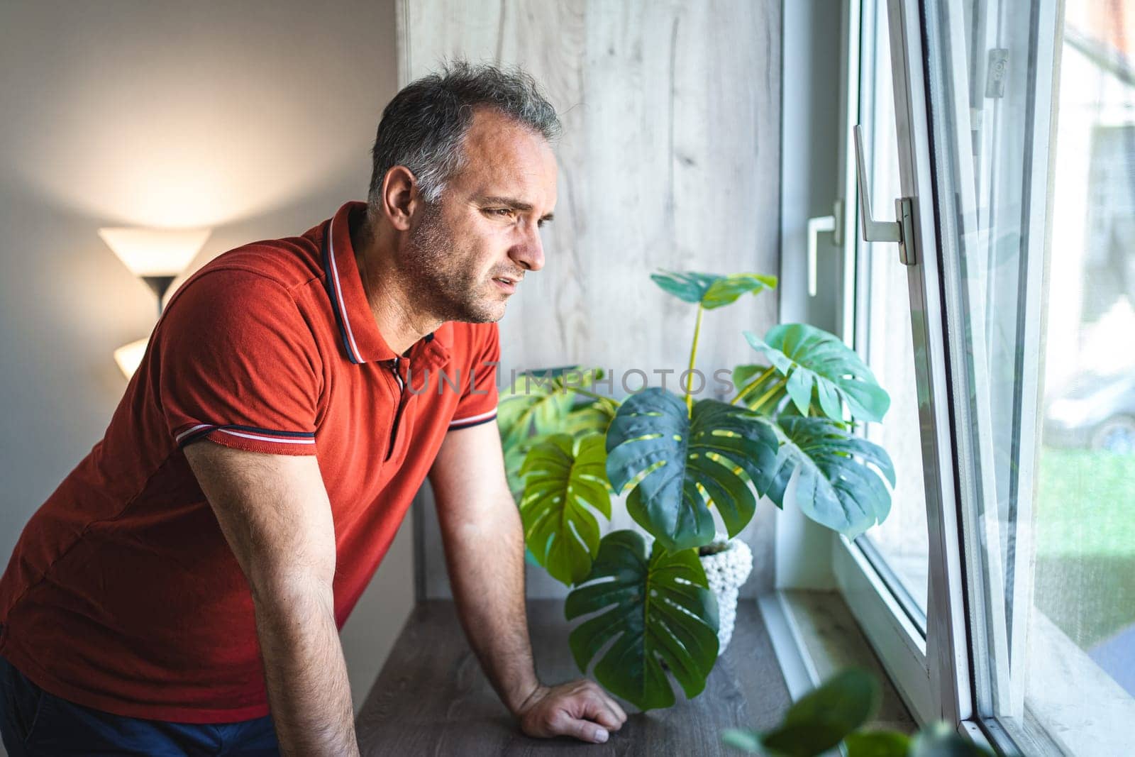 Man standing by the window looking sad and distraught.