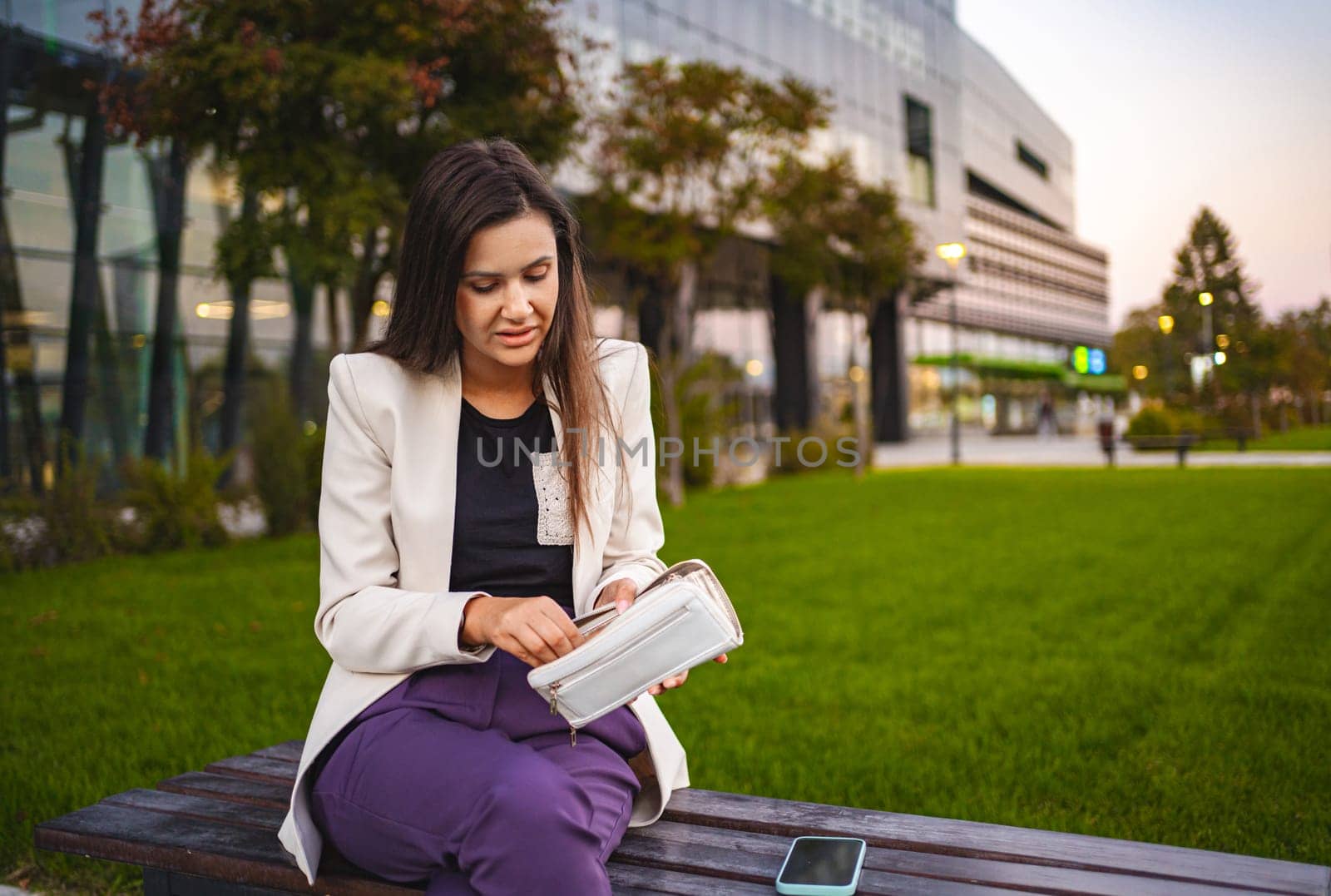 Businesswoman sitting at the park after work checking her wallet.
