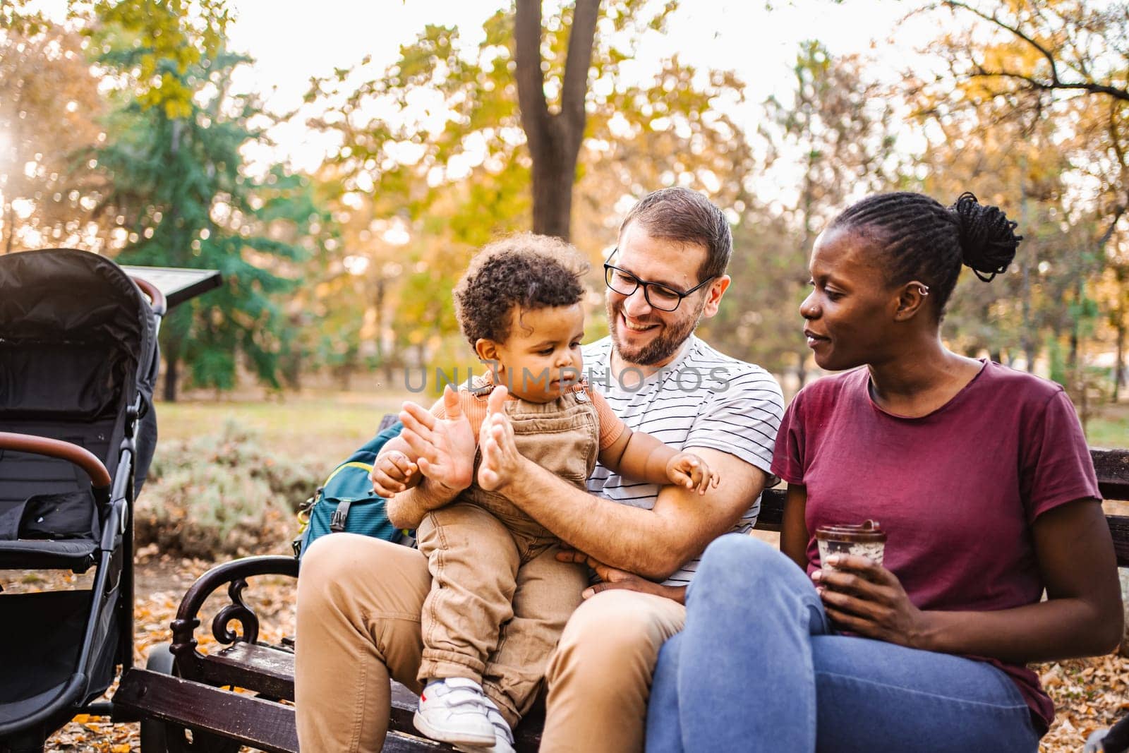 Mixed race couple is sitting on a park bench with their son.