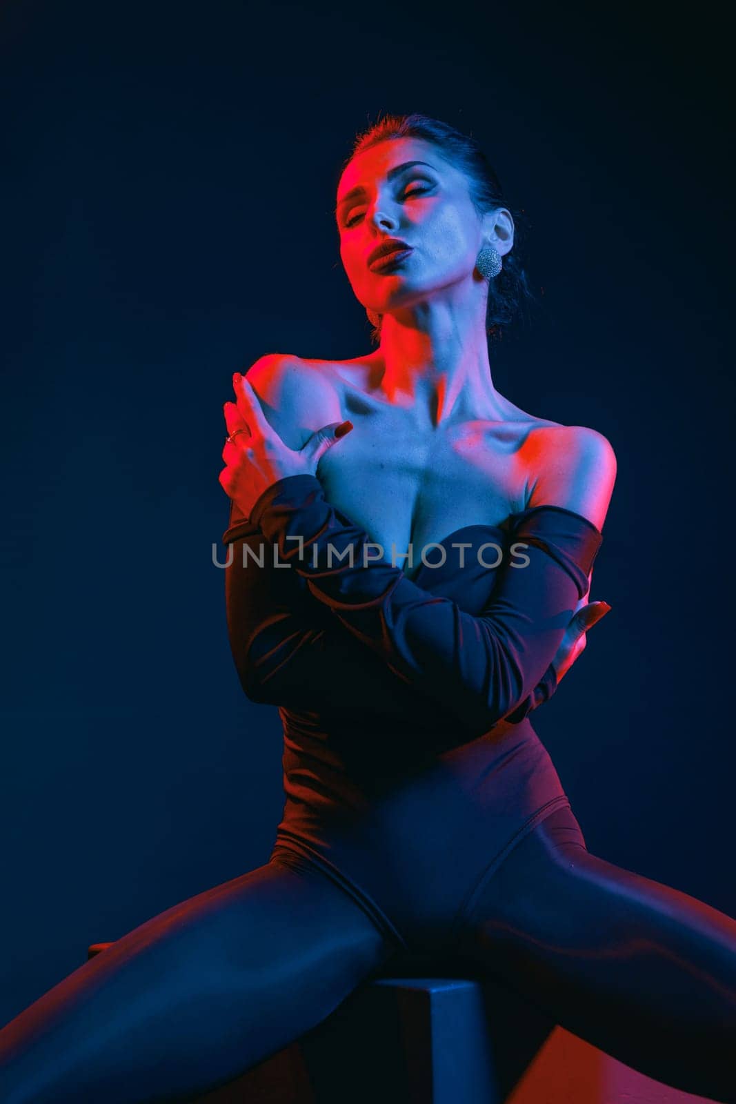 Glamorous woman in dramatic lighting posing in bodysuit, expressing confidence and sensual elegance in studio.