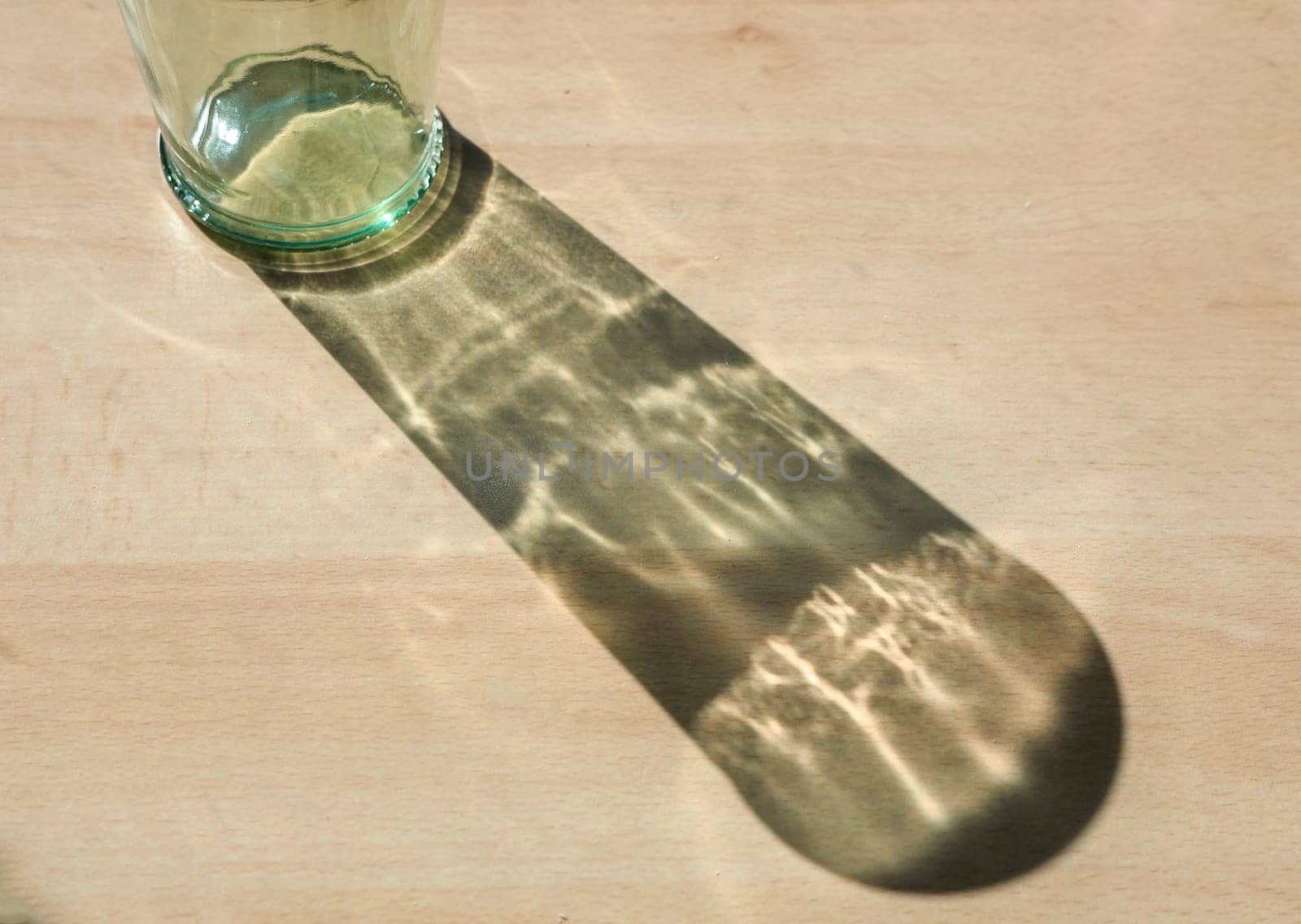 Empty glass bottle projecting an elongated shadow on a wooden surface, creating an interesting play of light and shadow