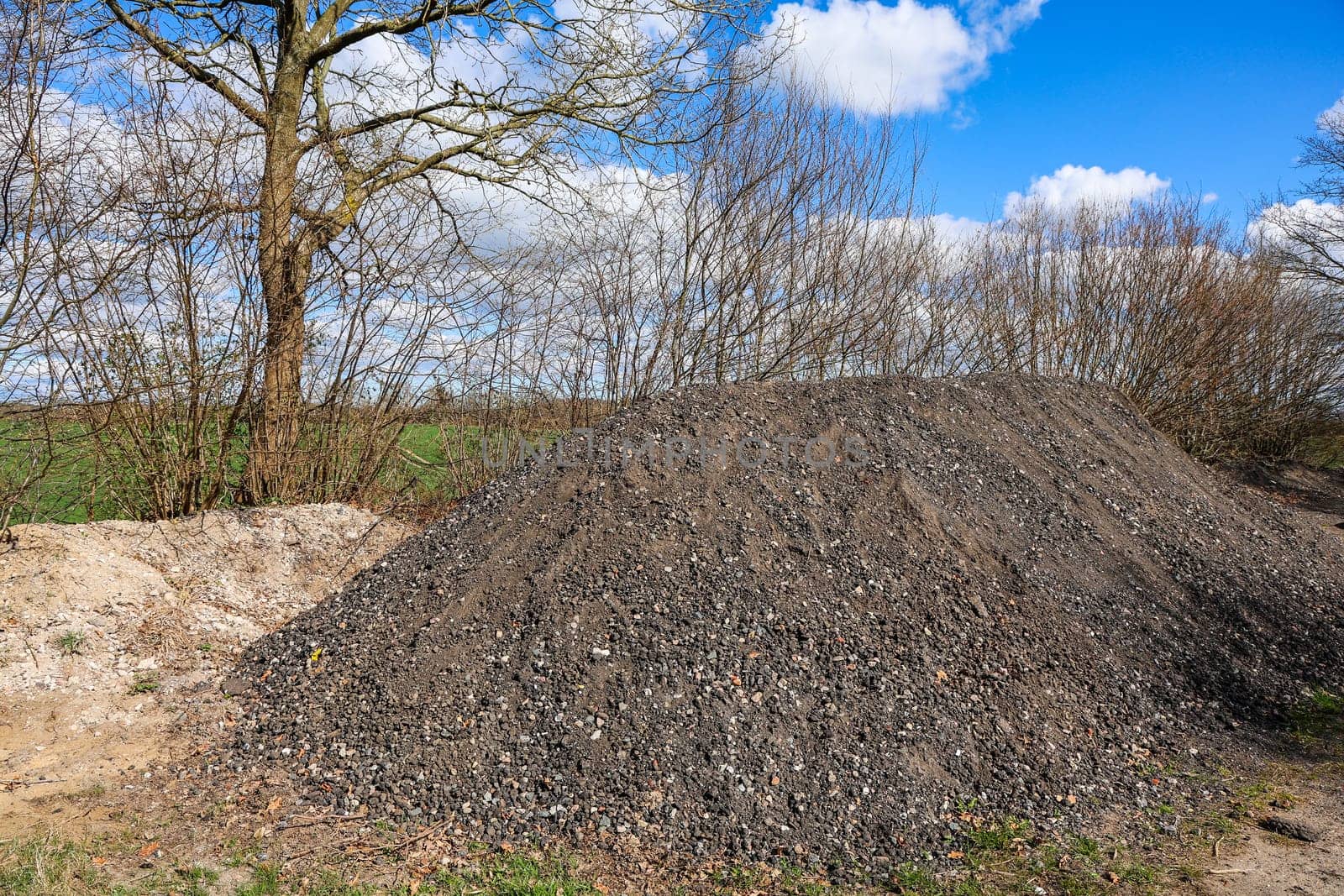 Gravel pile on a construction site with trees, bushes and a blue sky with clouds in background