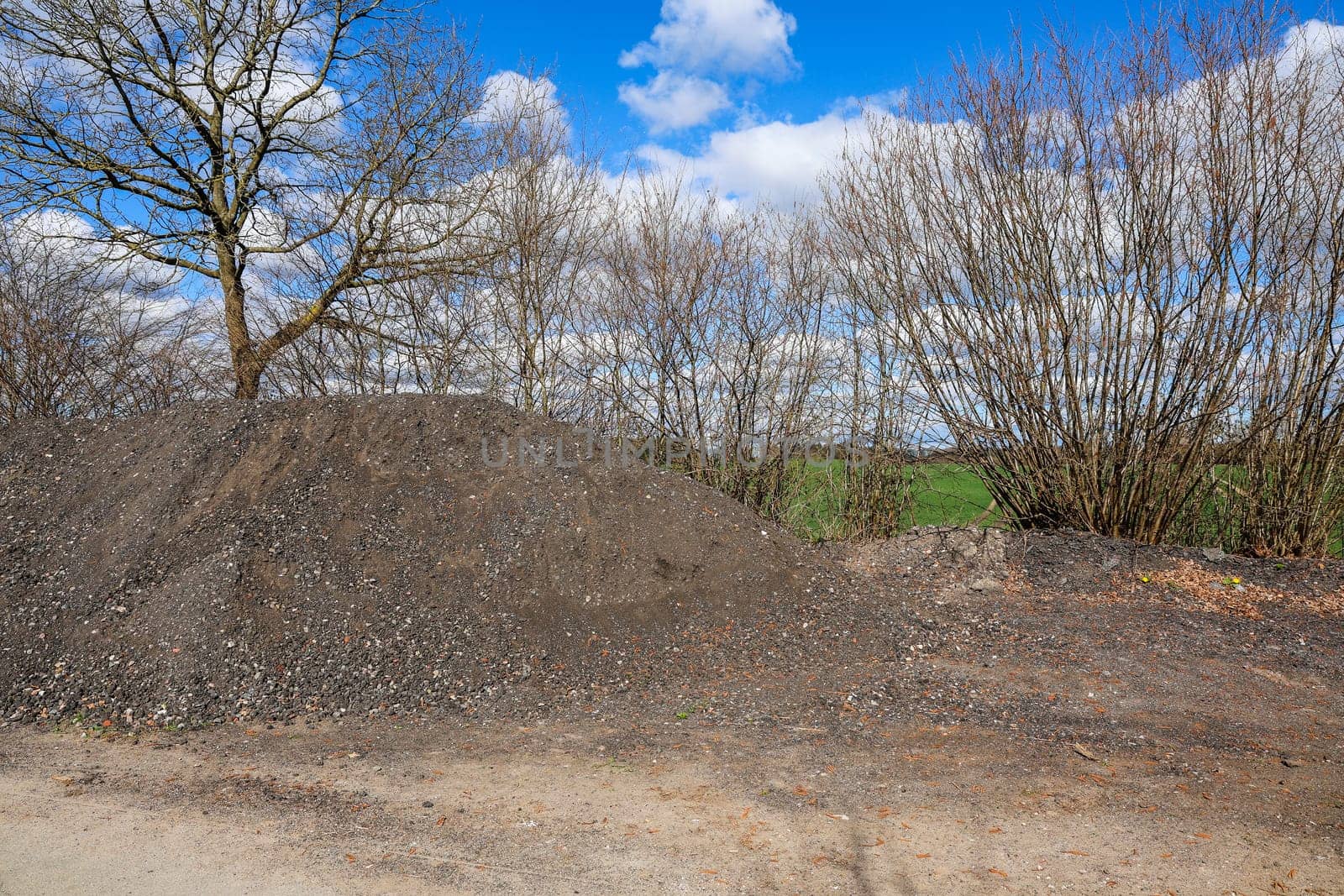 Gravel pile with trees and blue sky in the background, perfect for construction and landscaping projects