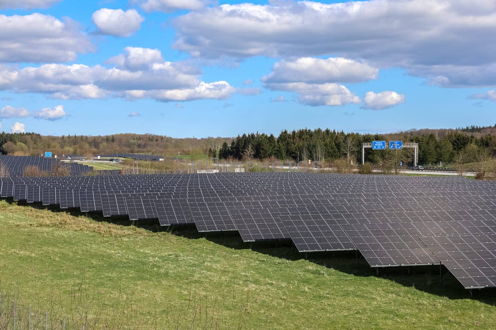 Large photovoltaic plant providing clean energy near a highway, under a cloudy sky in spring