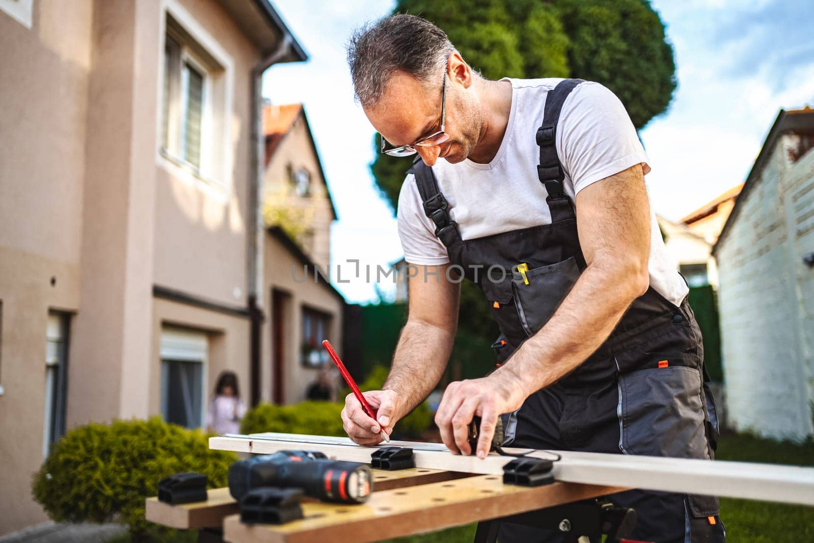 Mature male carpenter measuring wooden plank outdoors.