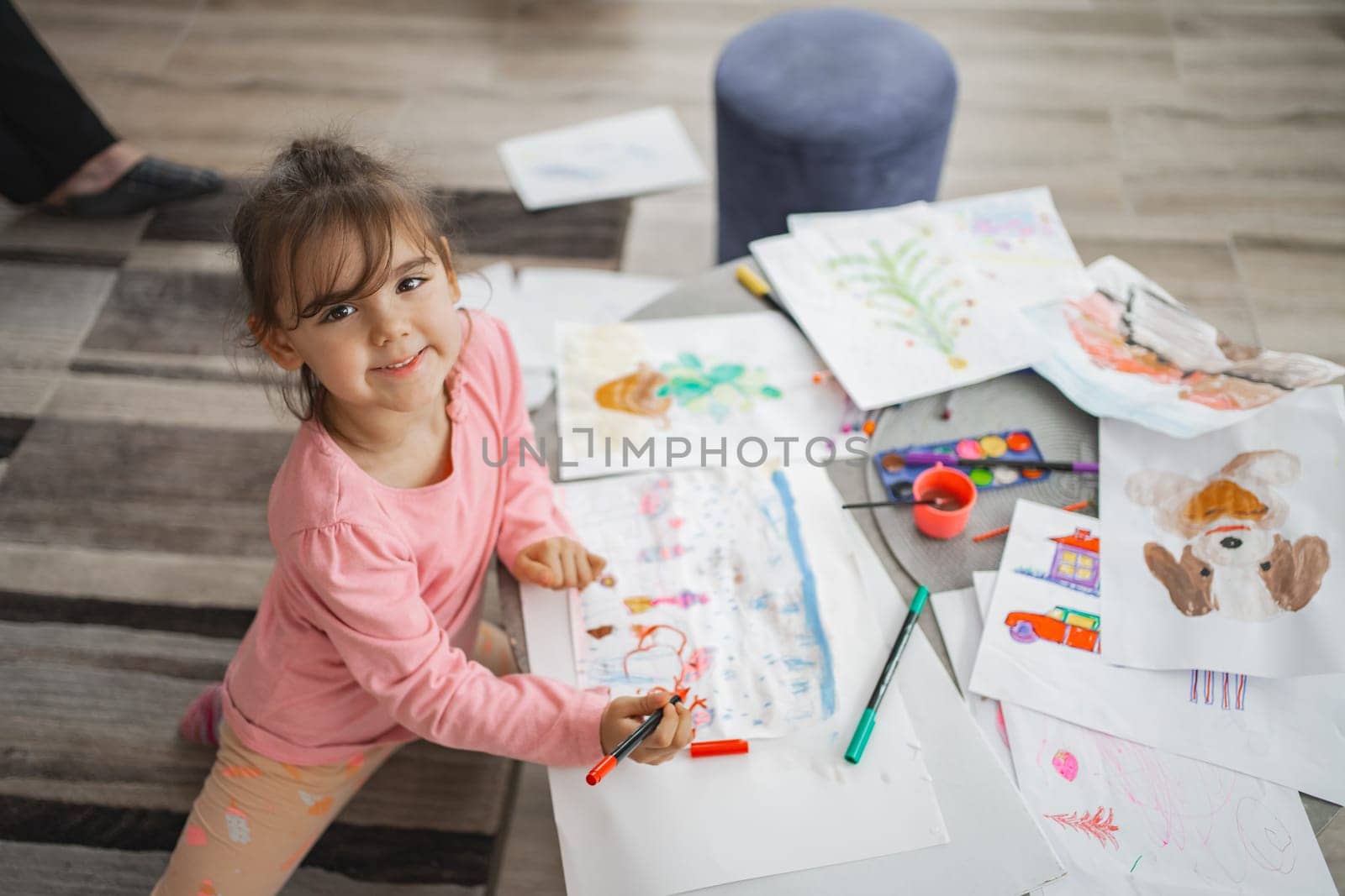 A cheerful child joyfully engages in colorful art creation on the floor.