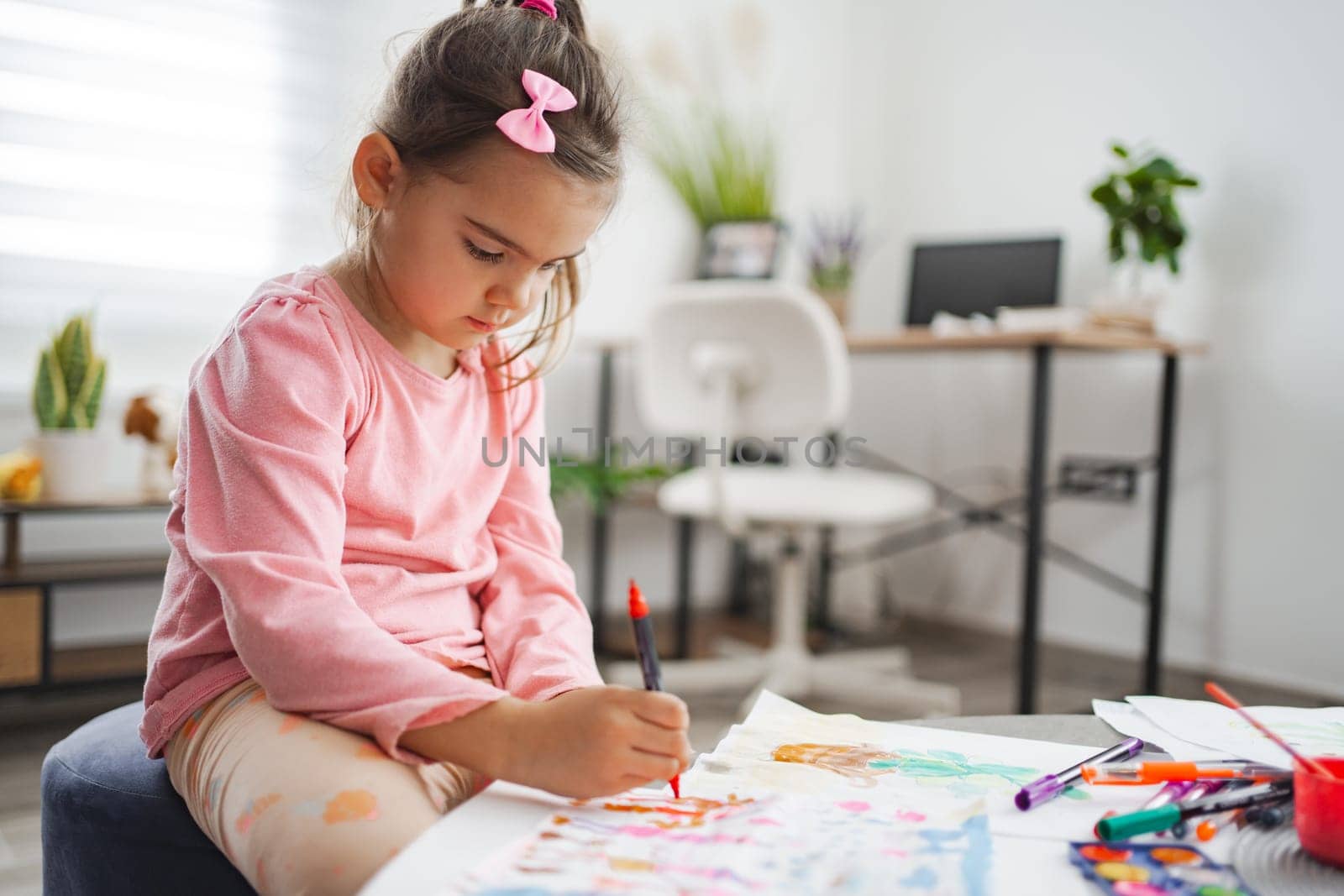 A child is deeply focused on drawing with vivid markers at her desk.