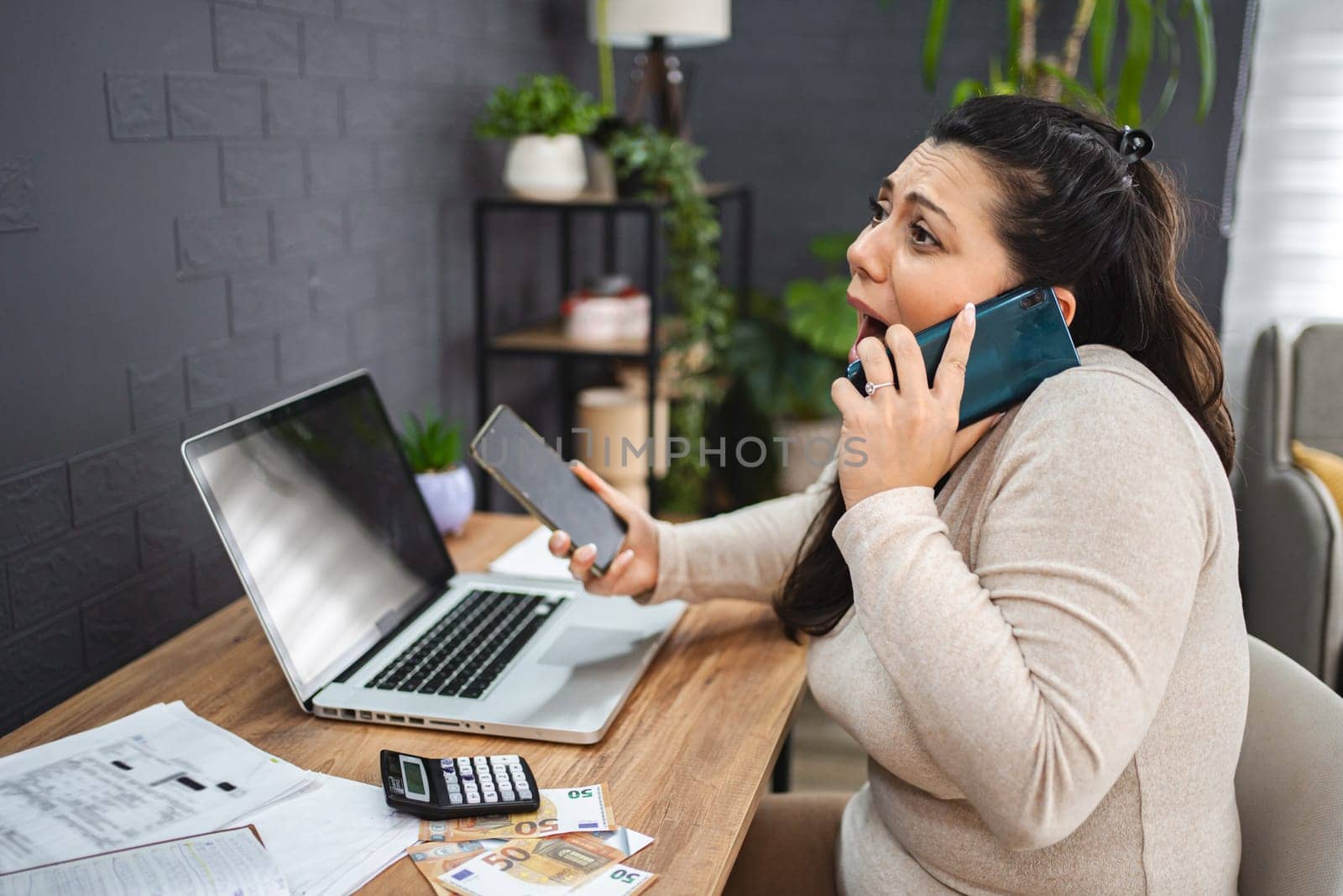 Frustrated woman talking on the phone while doing home finances.