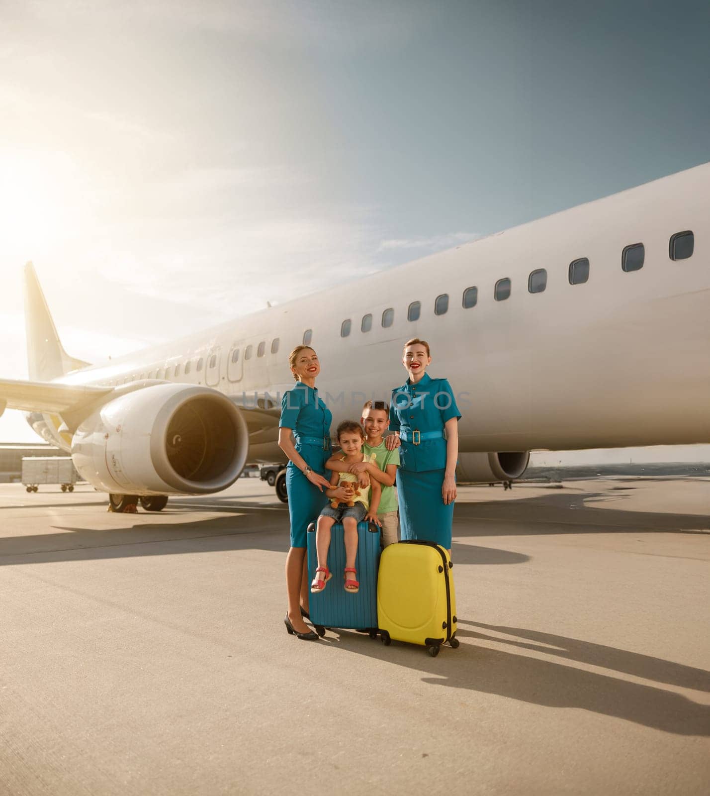 A happy and joyful family is seen interacting with friendly flight attendants next to a plane at the busy airport