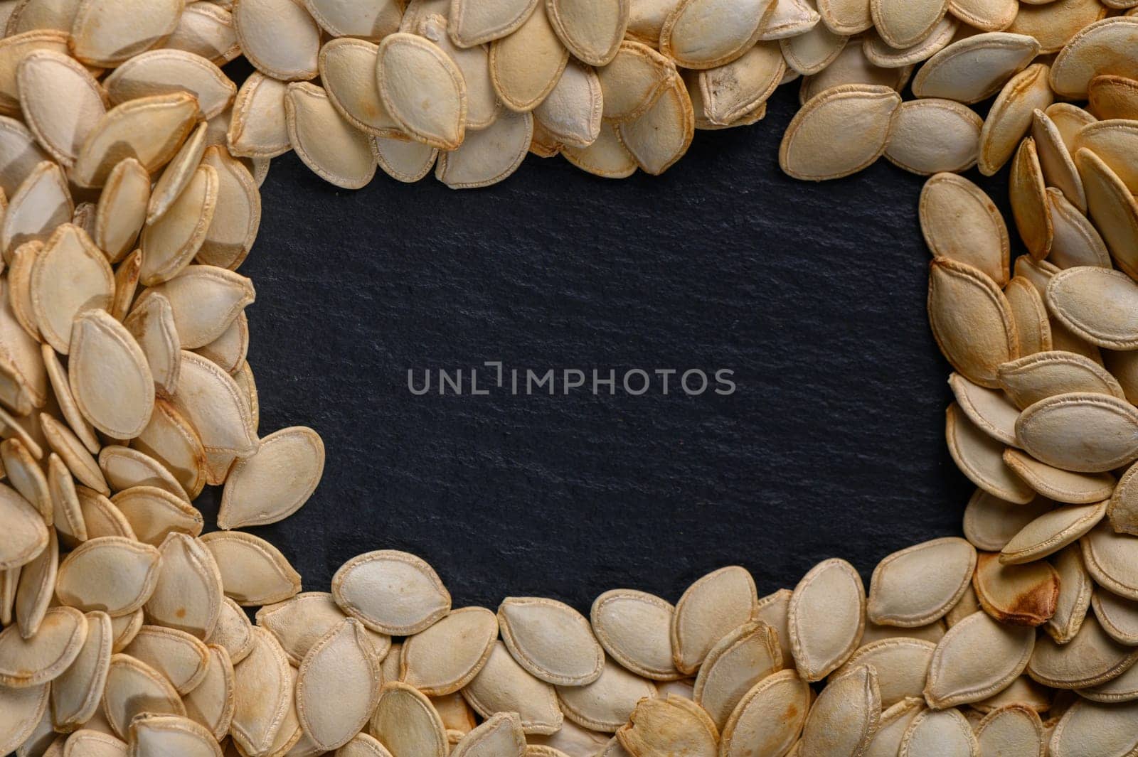 A stunning display of pumpkin seeds arranged neatly around a central dark slate area invites thoughts of autumn festivities and creative culinary uses. Perfect for seasonal decoration.