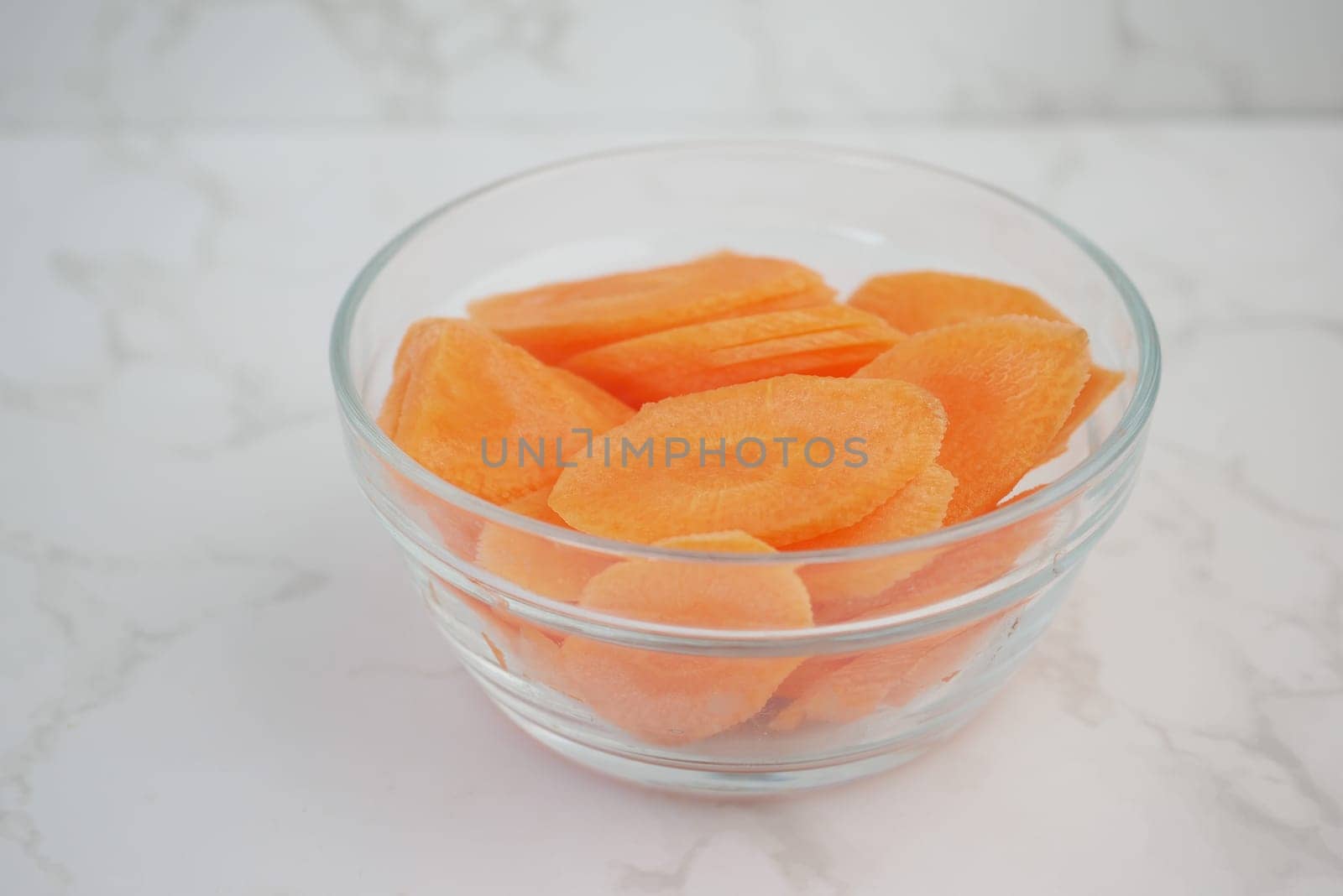 Bright orange carrot slices neatly arranged in a clear glass bowl on marble.