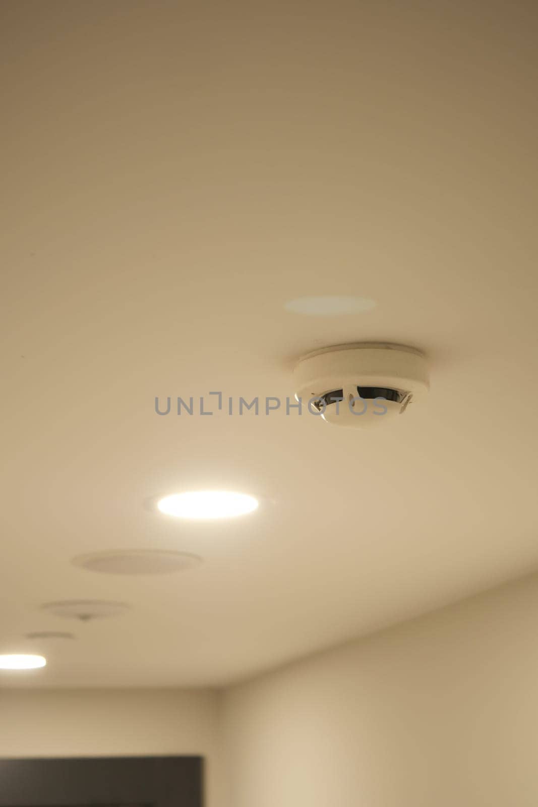 Bright ceiling lights illuminate a modern room with a smoke detector visible.