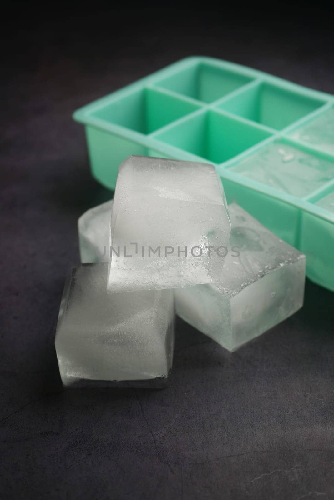 Three clear ice cubes are resting next to a mint green ice tray.