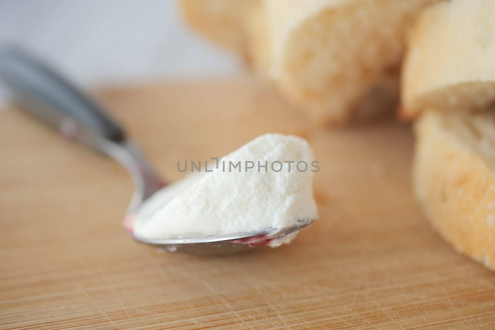 Creamy cheese spread sits on a spoon next to fresh bread slices.