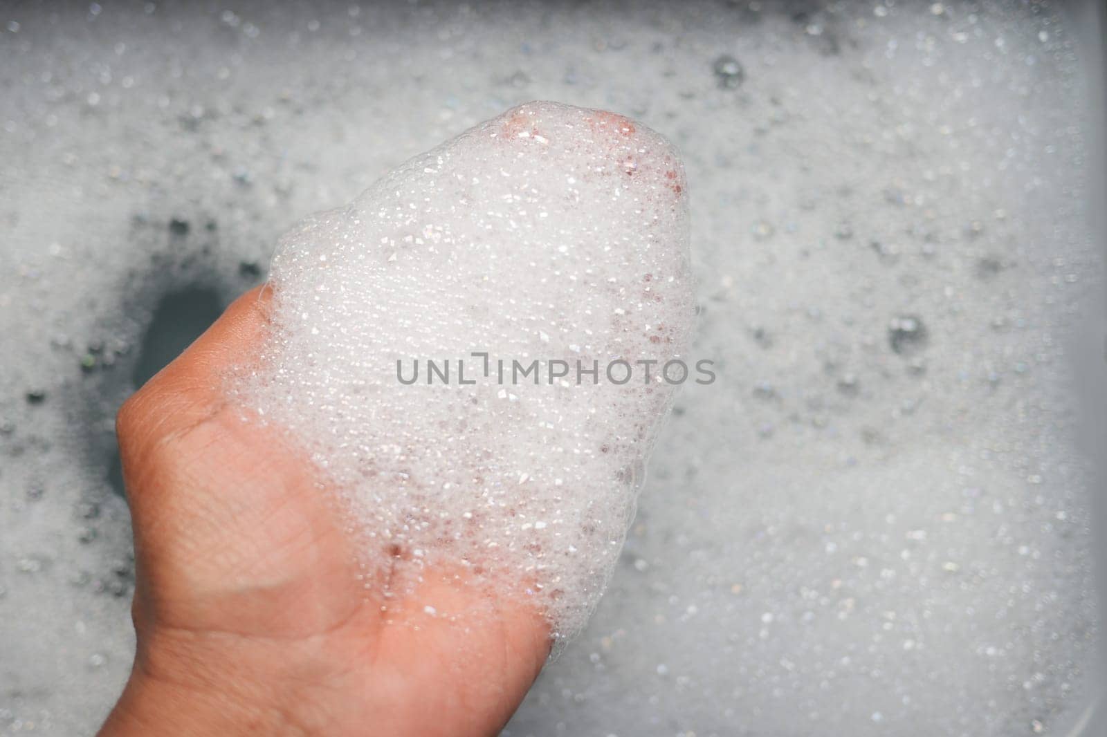 Soapy bubbles accumulate on a hand in warm, running water.