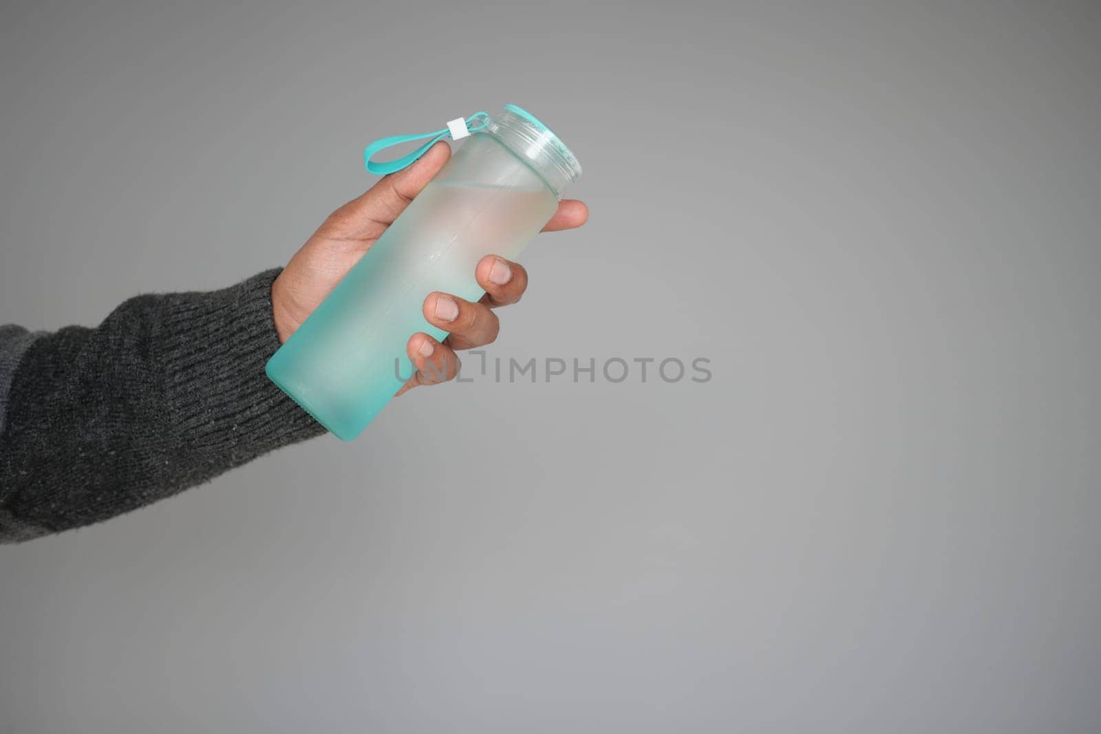 Person holds a clear water bottle with a turquoise lid and strap.