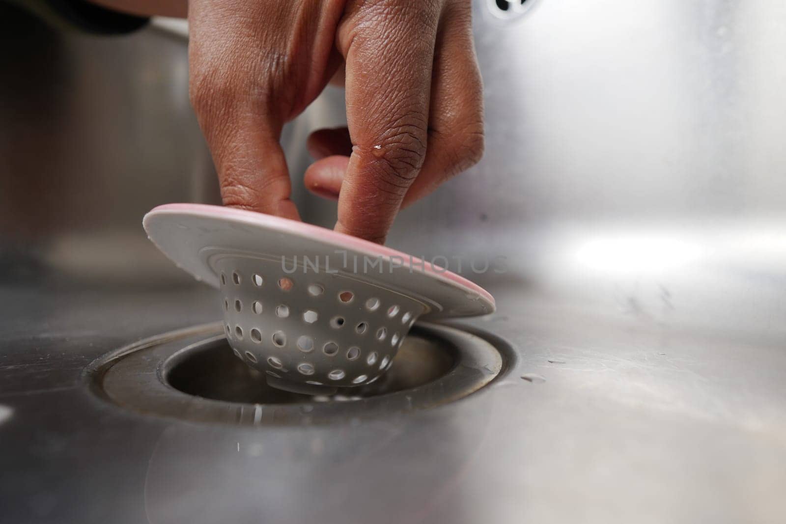 Hand is inserting a sink strainer into a drain to prevent clogging.