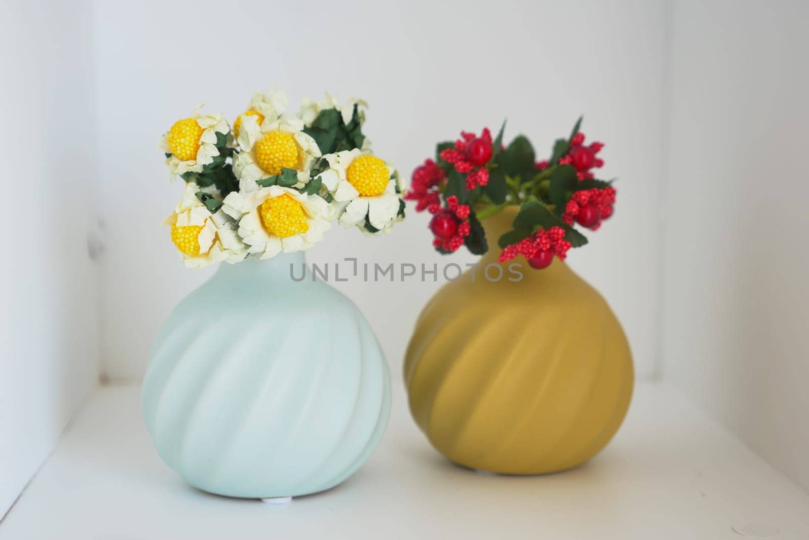 Two decorative vases hold vibrant flowers on a minimalist shelf.