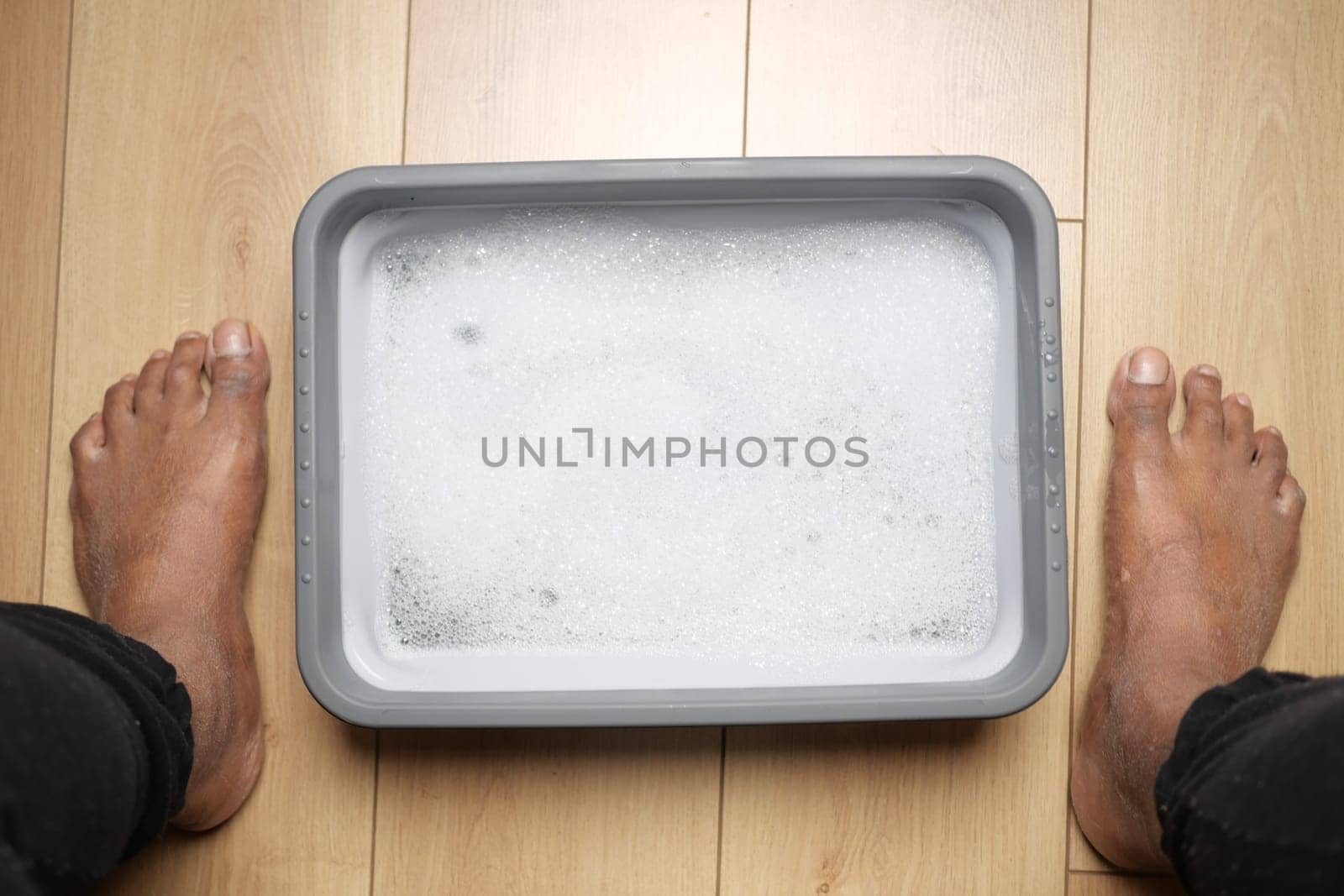 Bare feet soak in a bubbling container on wooden floor at home.