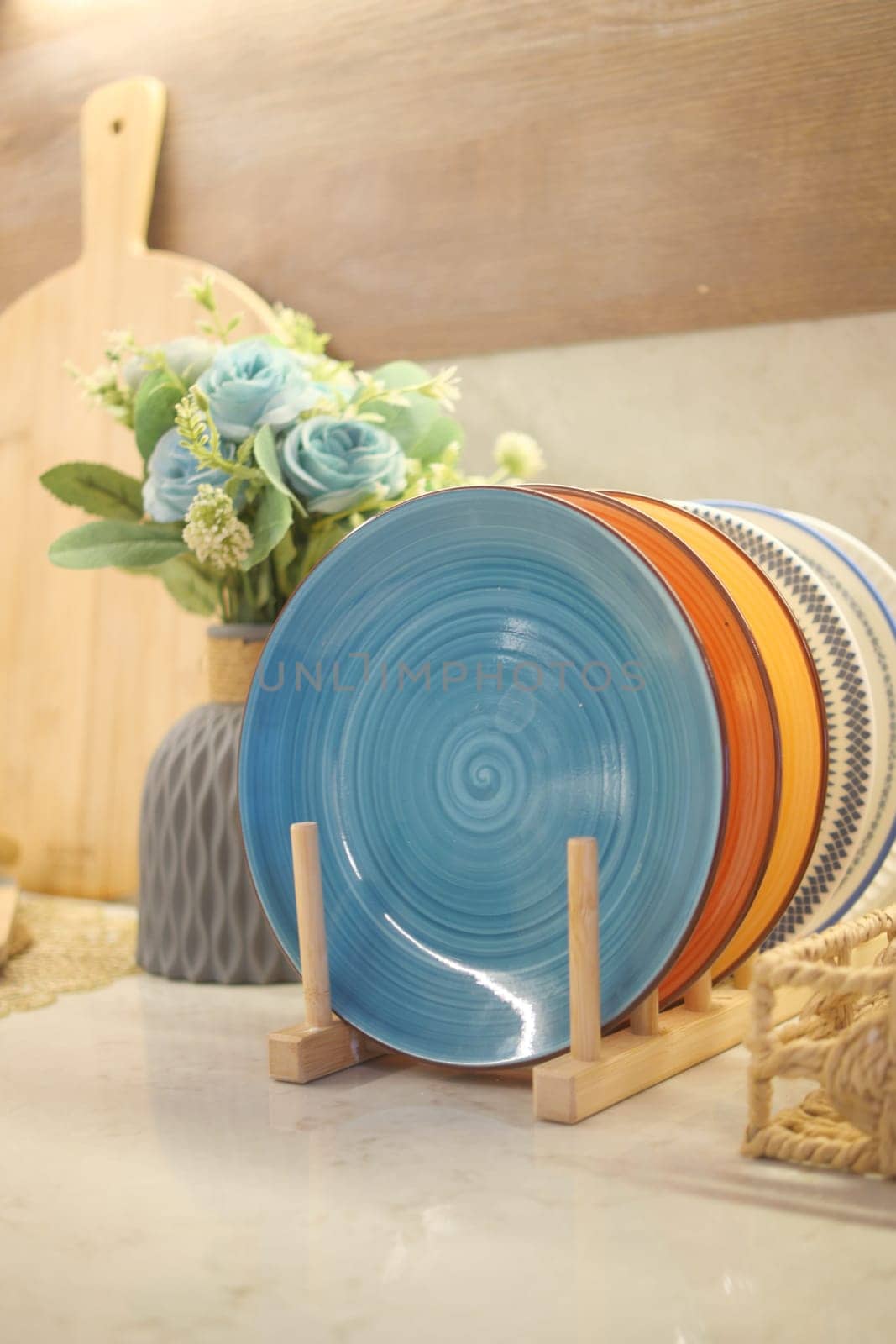 Brightly colored plates are arranged on a wooden stand beside vibrant flowers.