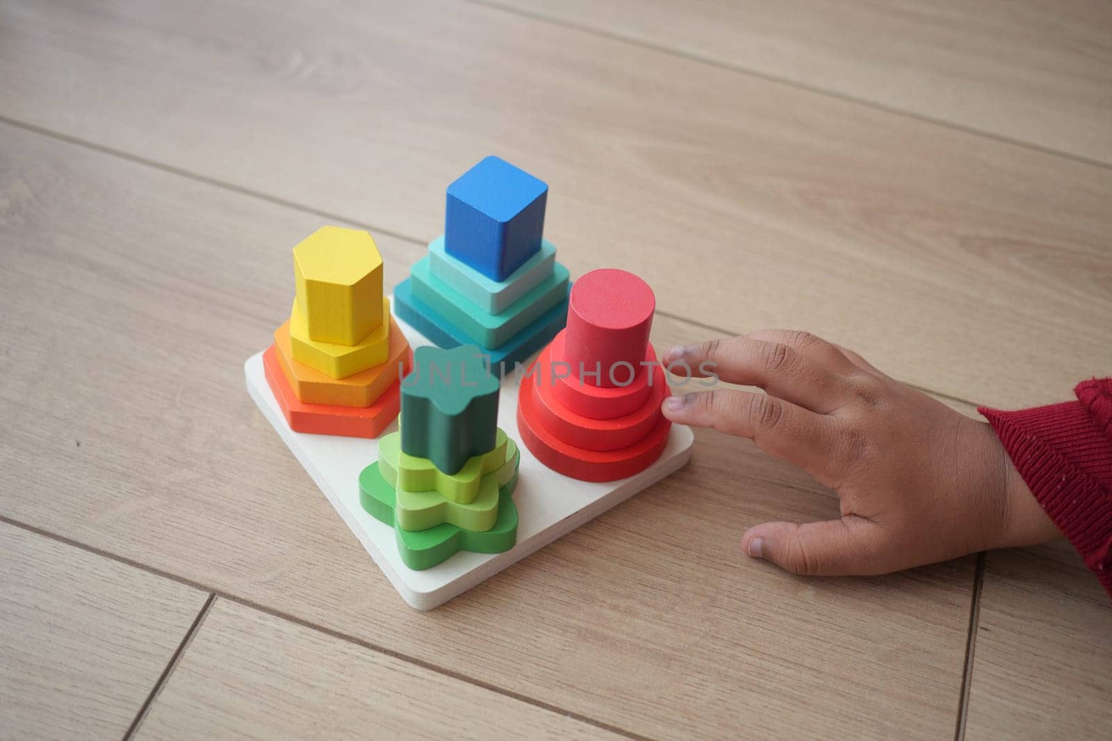 A child explores a vibrant stacking toy set on a wooden floor.