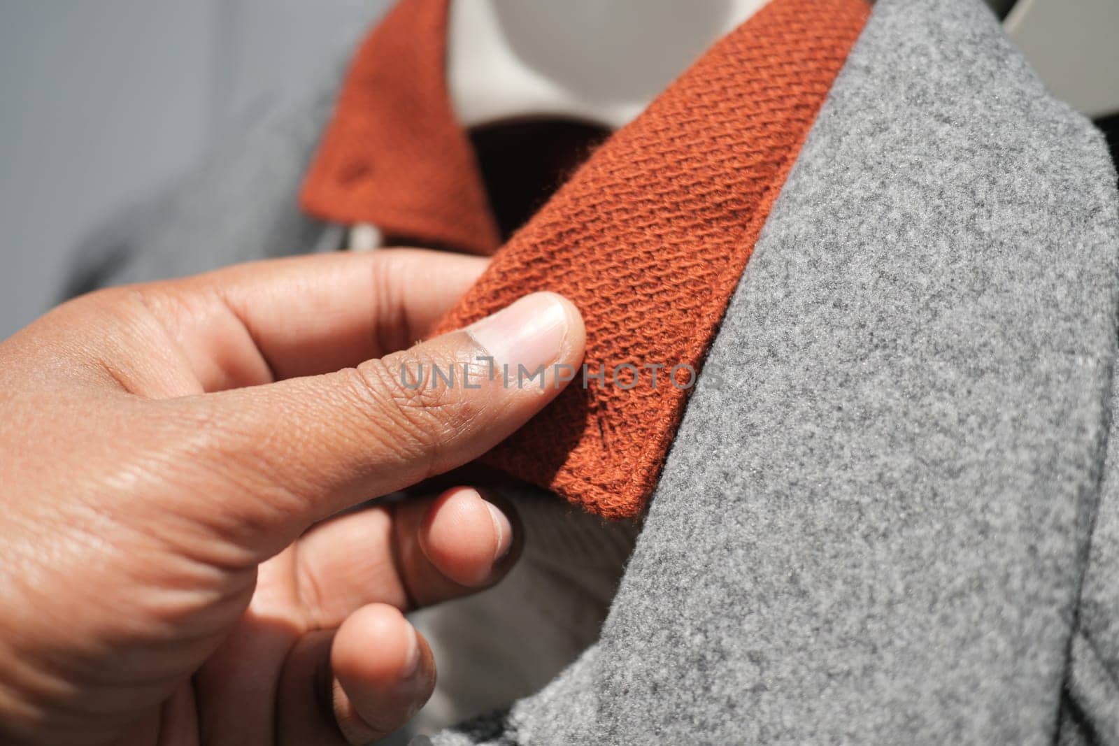 A hand is inspecting the collar of a gray coat featuring a rust-colored detail.