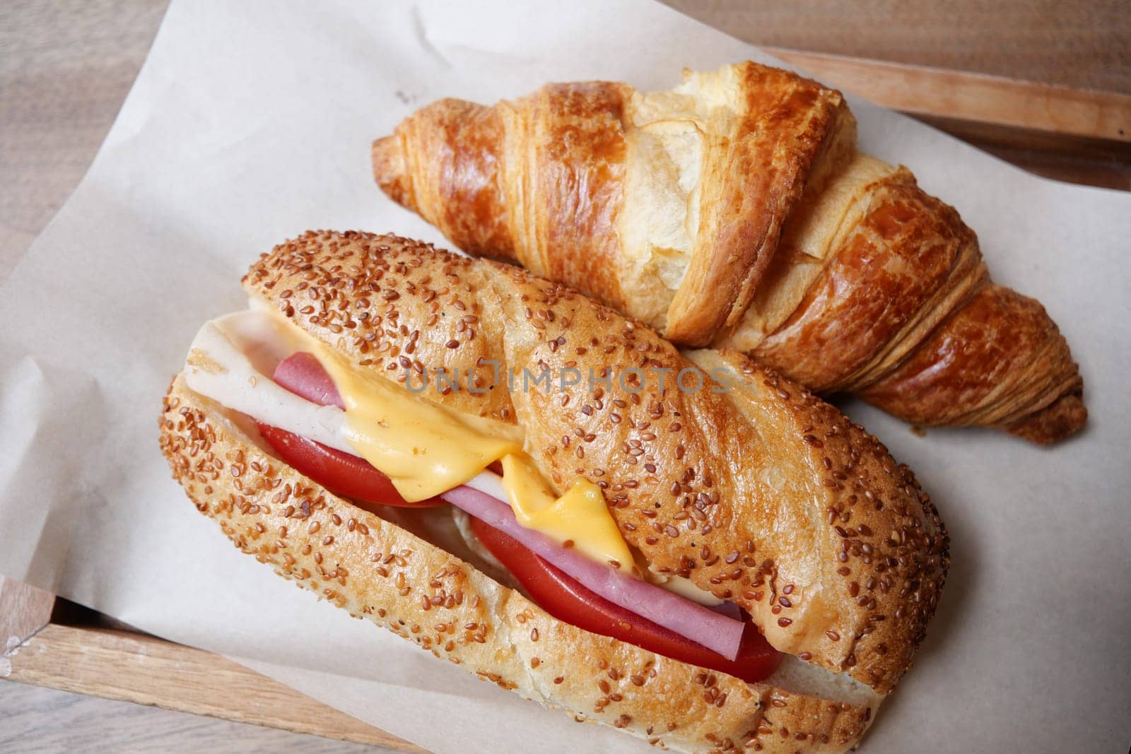Delicious croissant and sandwich with ham, cheese, and tomato on a tray.