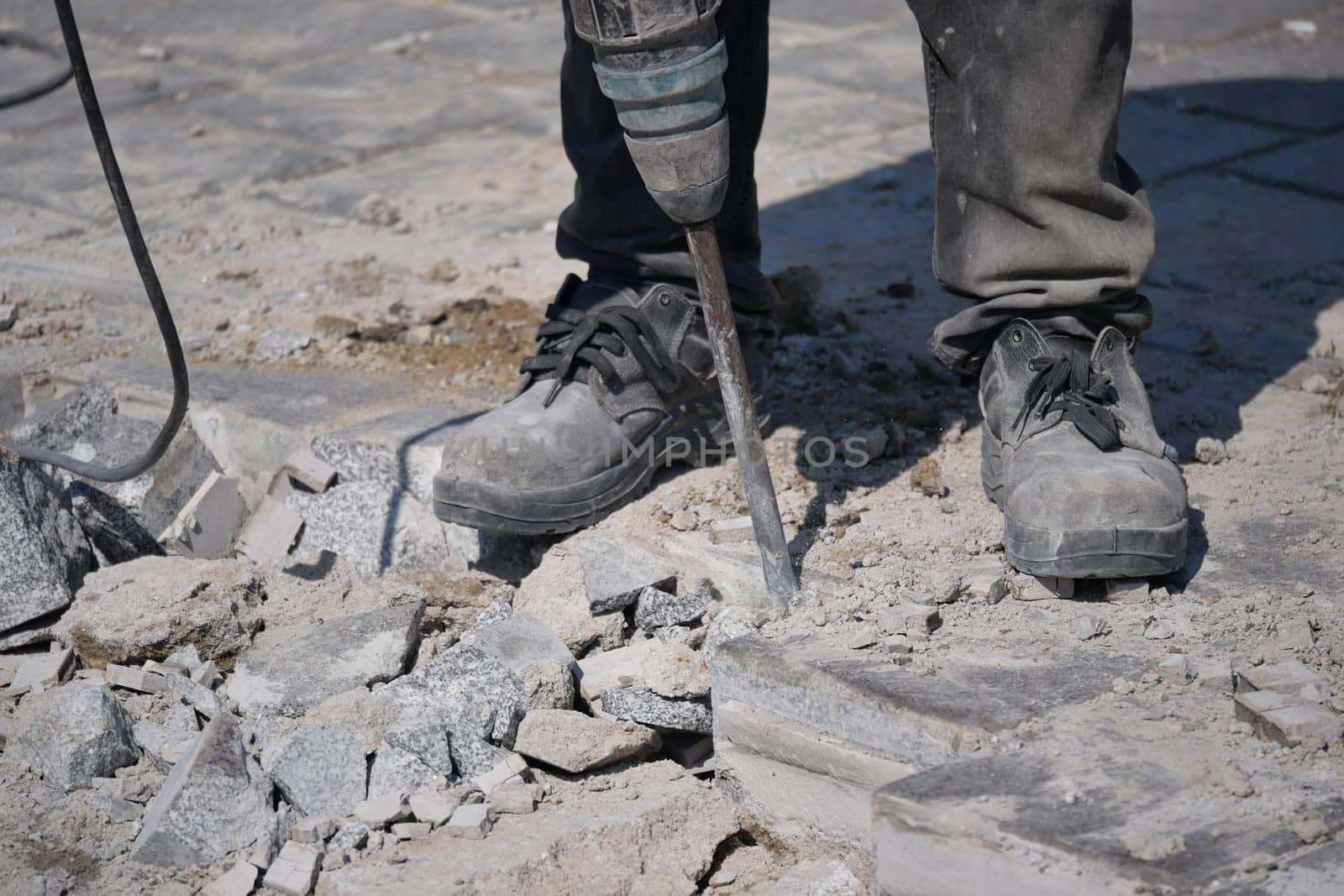 A construction worker breaks concrete using a pneumatic tool outdoors.