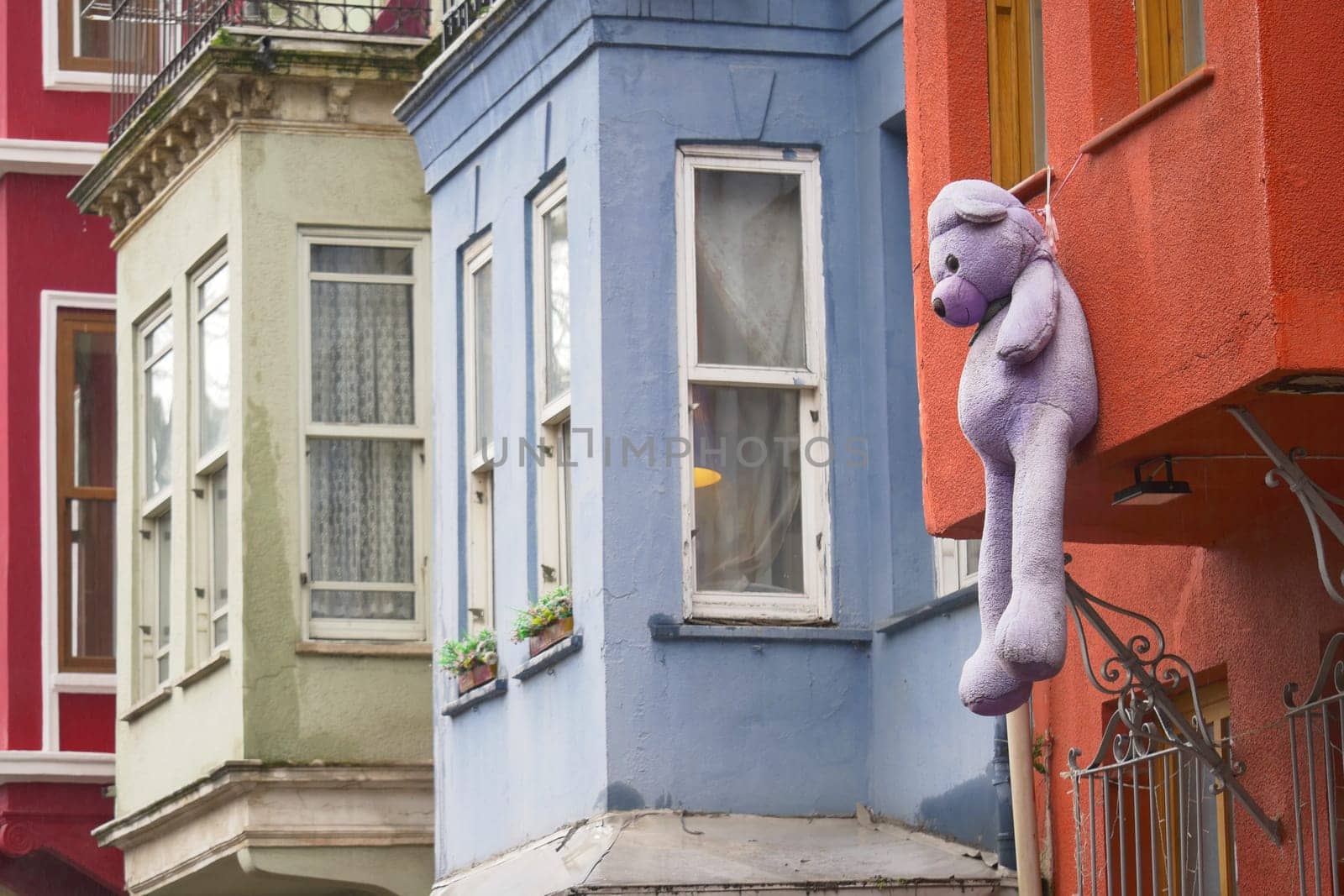 A large purple teddy bear hangs from a vibrant building in a city.