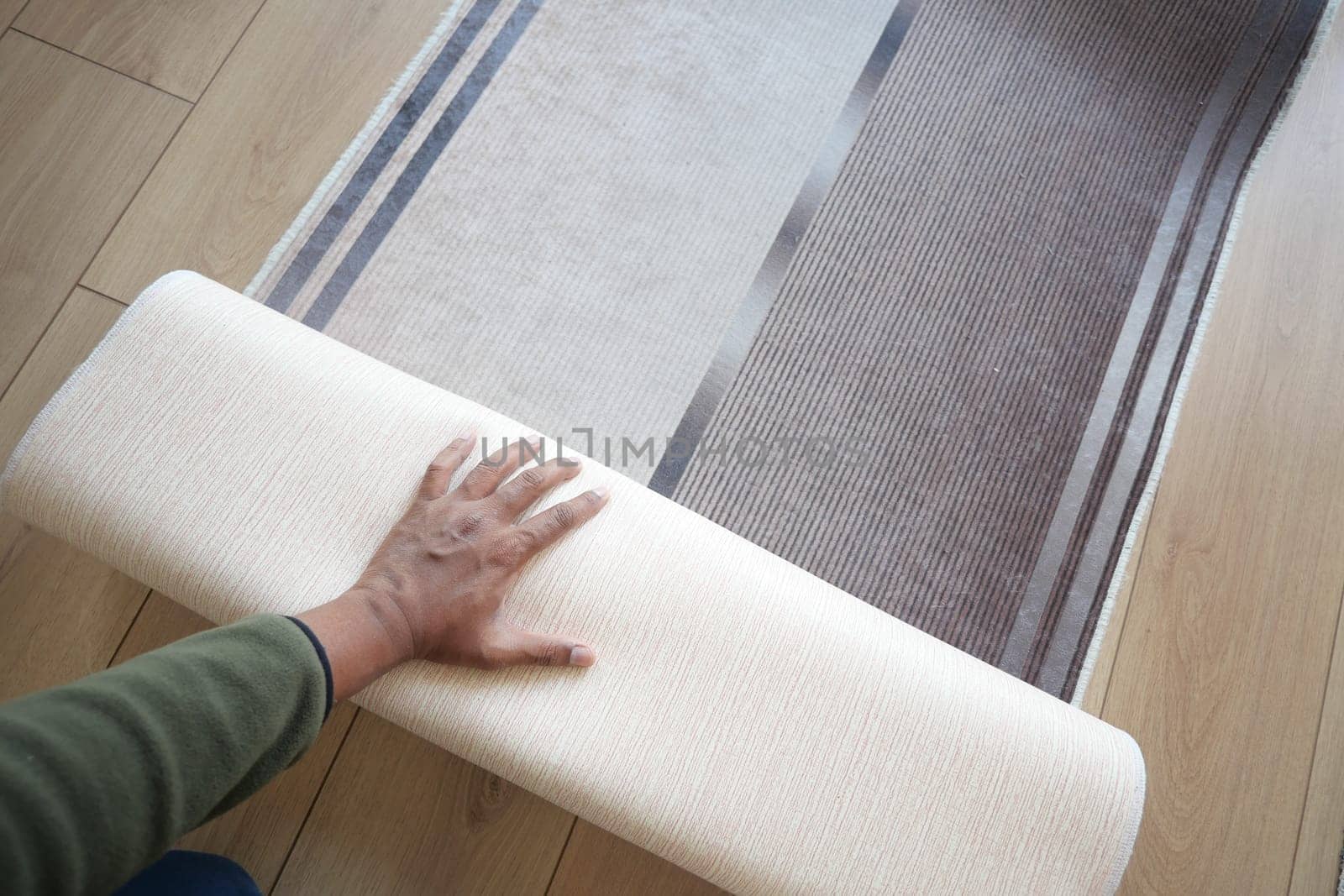 Person is unrolling a soft rug in a cozy living space to enhance decor.