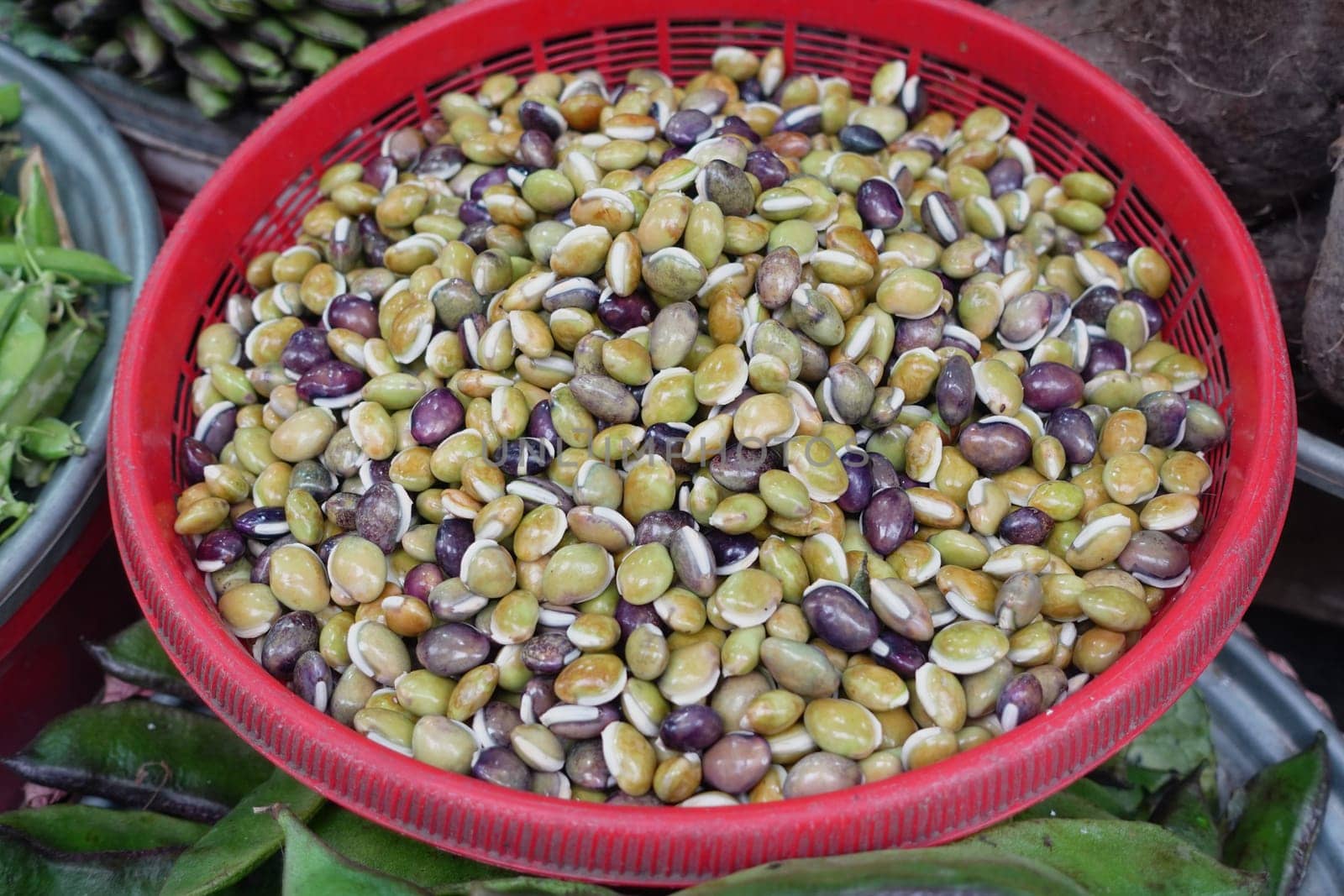 Freshly harvested beans in various colors fill a woven basket at a market.