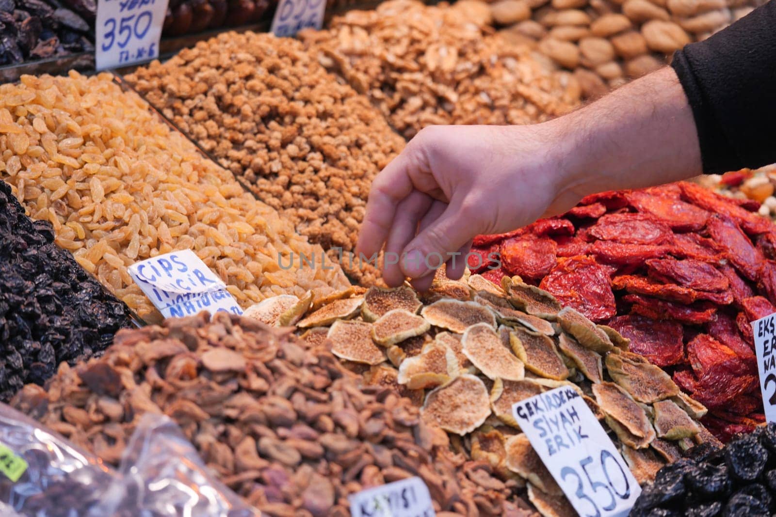 A person is selecting dried fruits and nuts at an outdoor market.