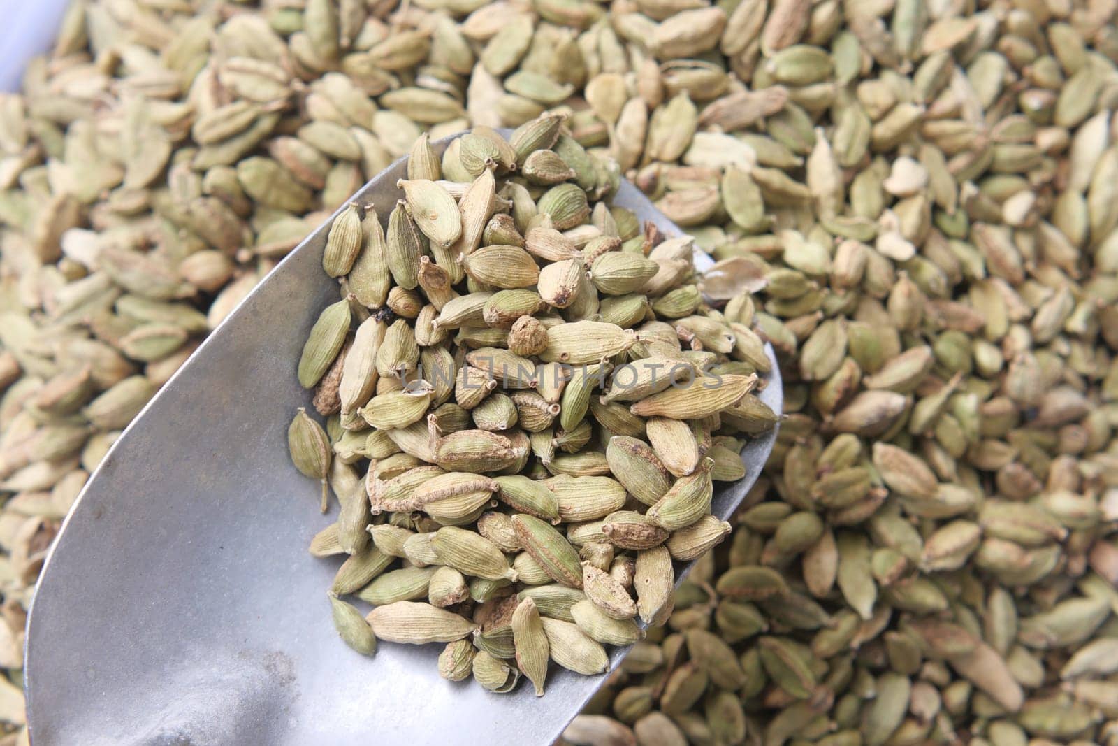 Green cardamom pods are shown in a metal scoop at a spice market.