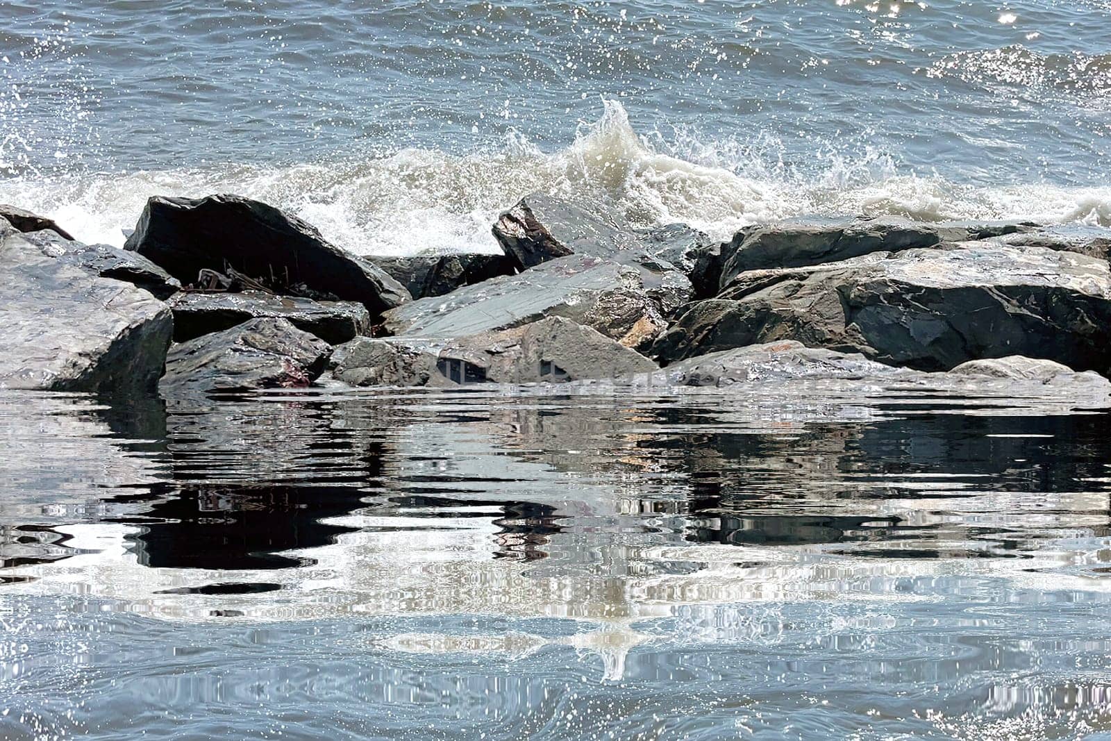 A scenic view of ocean waves splashing against rugged coastal rocks with sparkling water reflections under bright sunlight. Perfect for themes related to nature, tranquility, seaside, and travel.